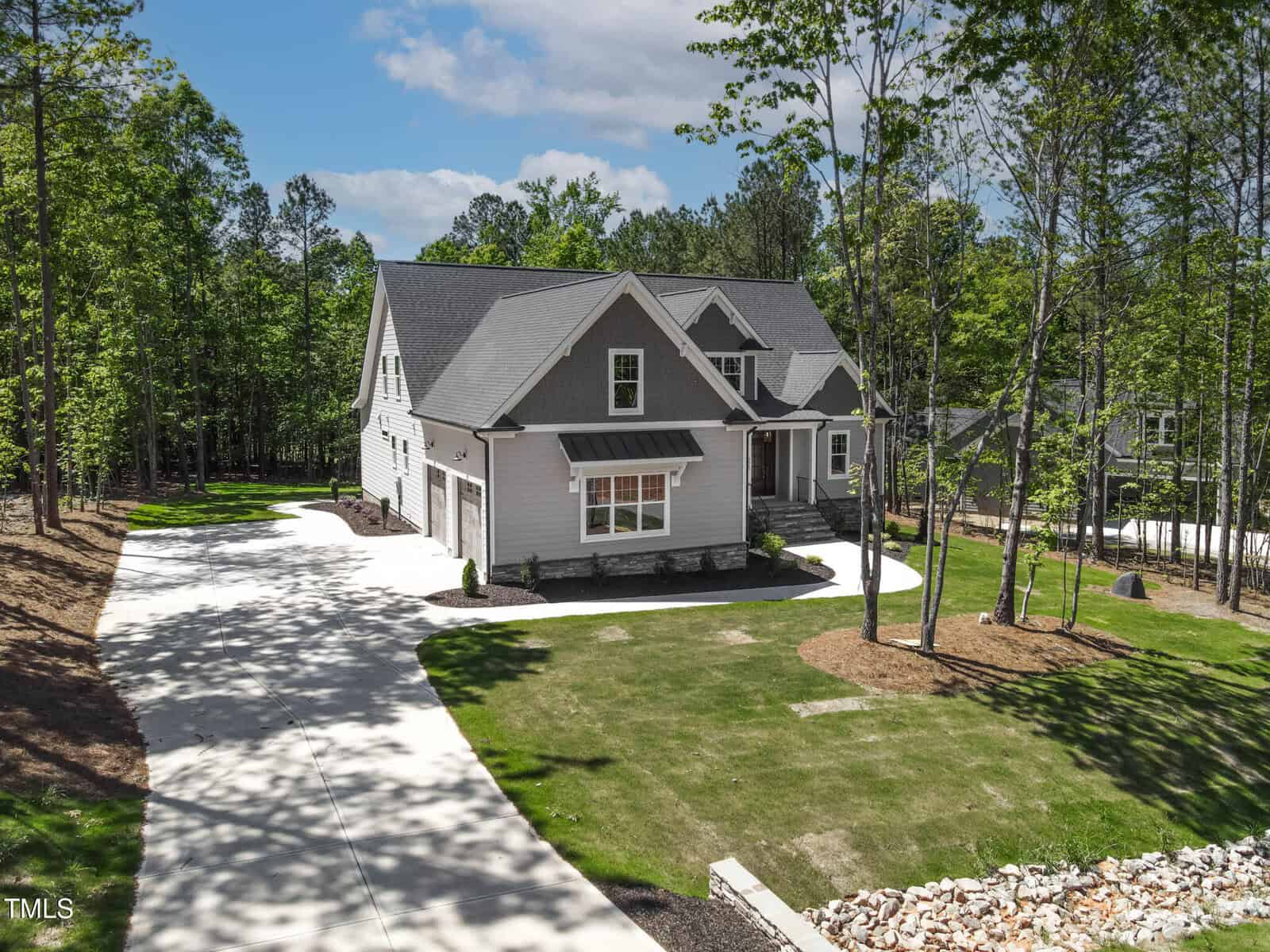 Located at 3923 Cedar Knolls Drive in Youngsville, this two-story gray house with white trim sits on a spacious lot with a well-maintained lawn, surrounded by trees. A long driveway leads to the attached garage under a partly cloudy sky.