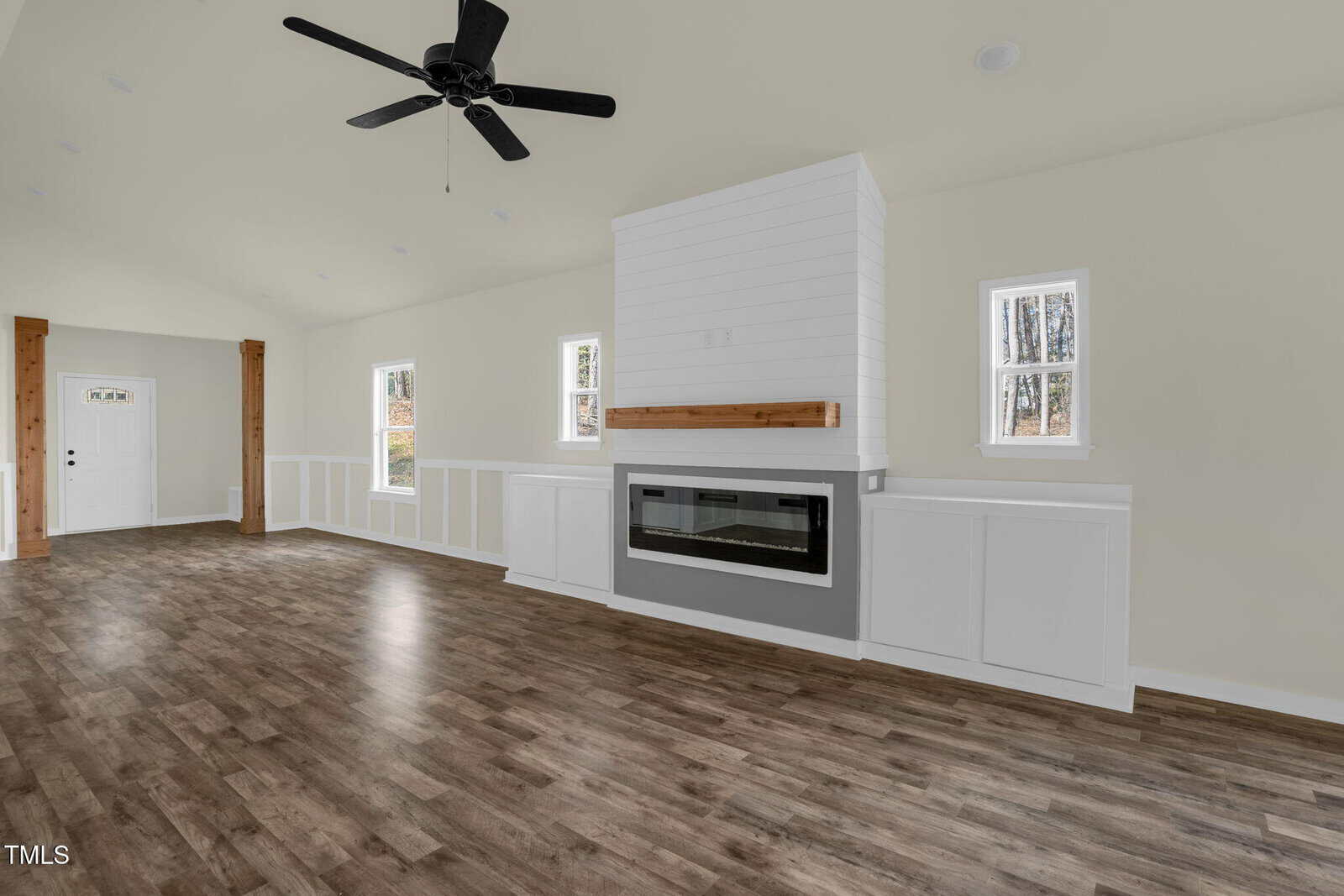 Spacious living room with wood floors, fireplace with a wood mantel, built-in cabinets, small windows, ceiling fan, and entry door with sidelights. White walls and trim throughout.