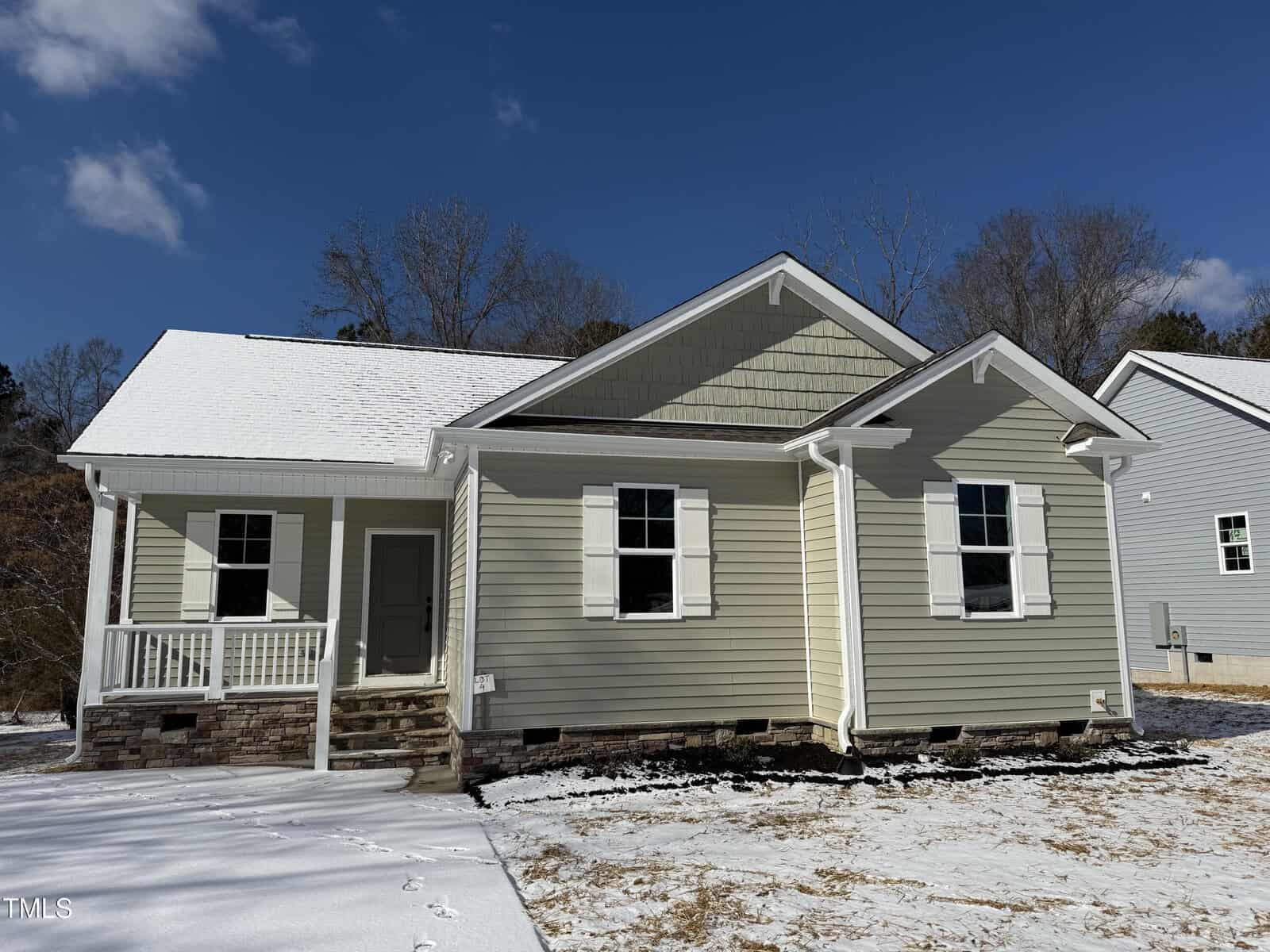 A charming single-story house at 117 Daniel Street in Oxford showcases light gray siding and a white roof. The inviting front porch, accessible by stairs, is complemented by a light dusting of snow on the ground, while the sky remains clear and blue.