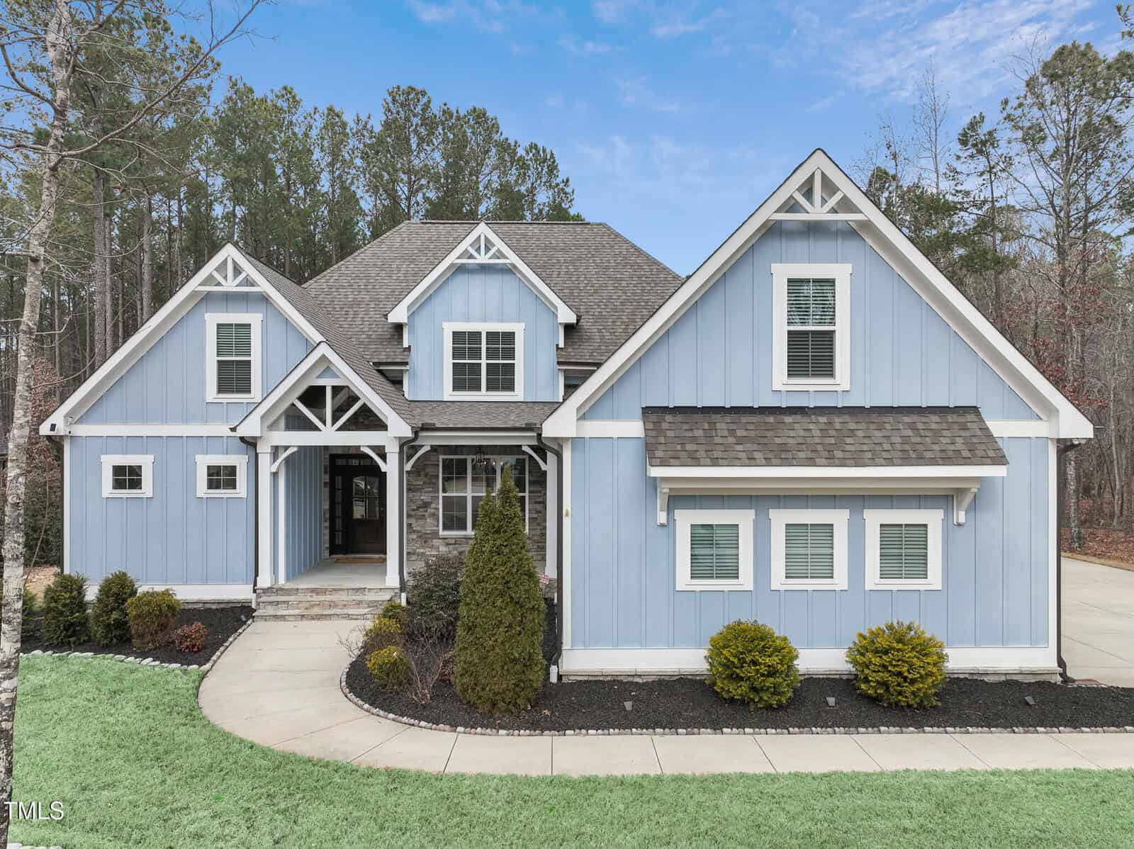 Nestled at 1205 Smith Creek Way in Wake Forest, this charming blue and white two-story house boasts a gabled roof, large front windows, and a covered entryway. Surrounded by trees, it features a neatly maintained lawn and a concrete driveway.