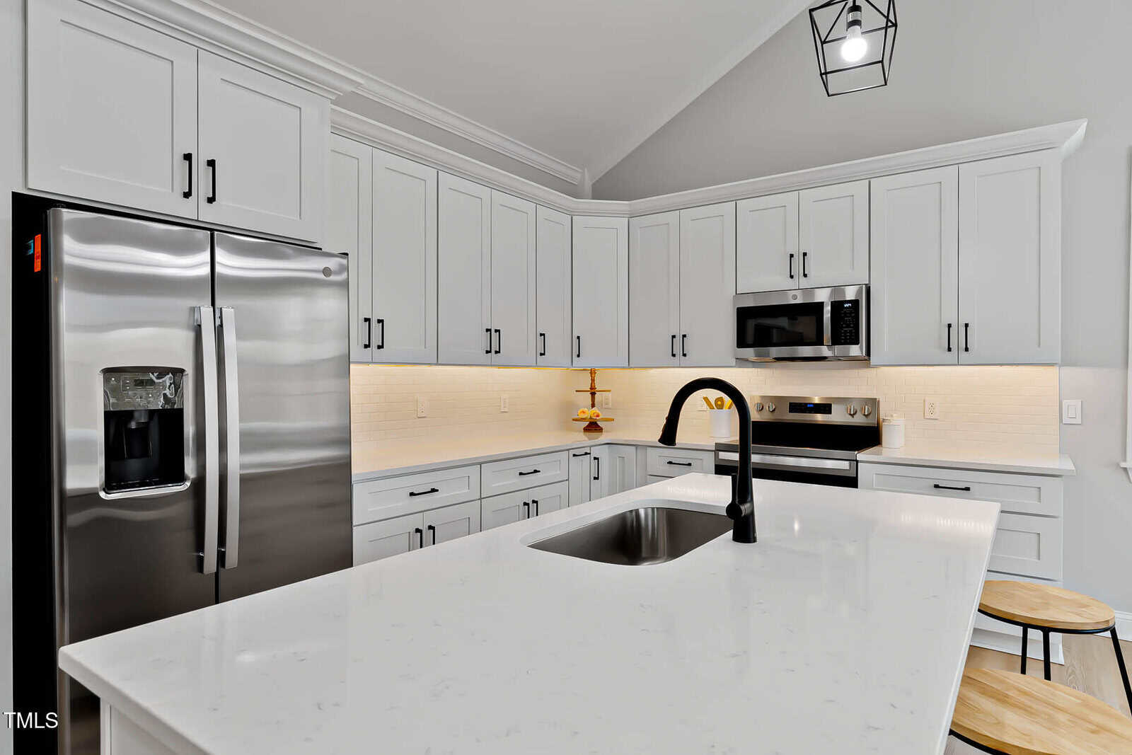 Modern kitchen with white cabinets, stainless steel appliances, an island with a sink and black faucet, under-cabinet lighting, and two wooden stools. Neutral color palette with clean, minimalist design.