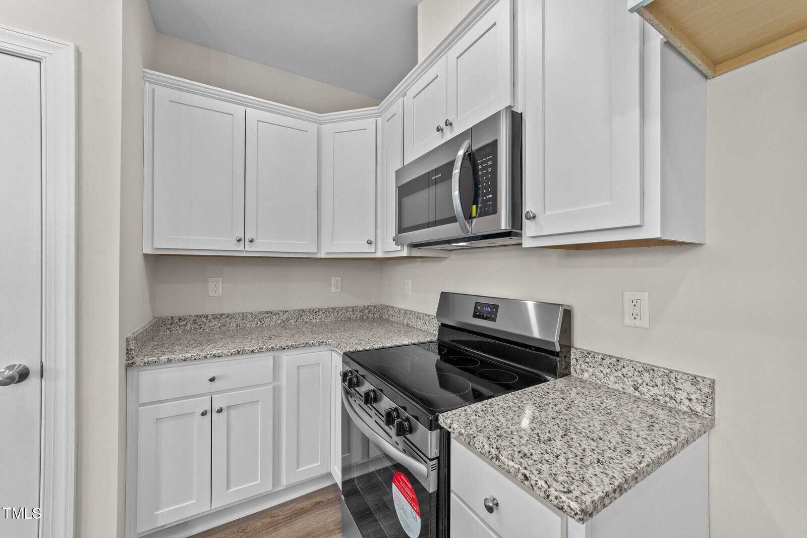 A modern kitchen with white cabinets, granite countertops, a stainless steel electric stove, and a matching over-the-range microwave. The walls are light-colored, and the floor appears to be wood or wood-look material.