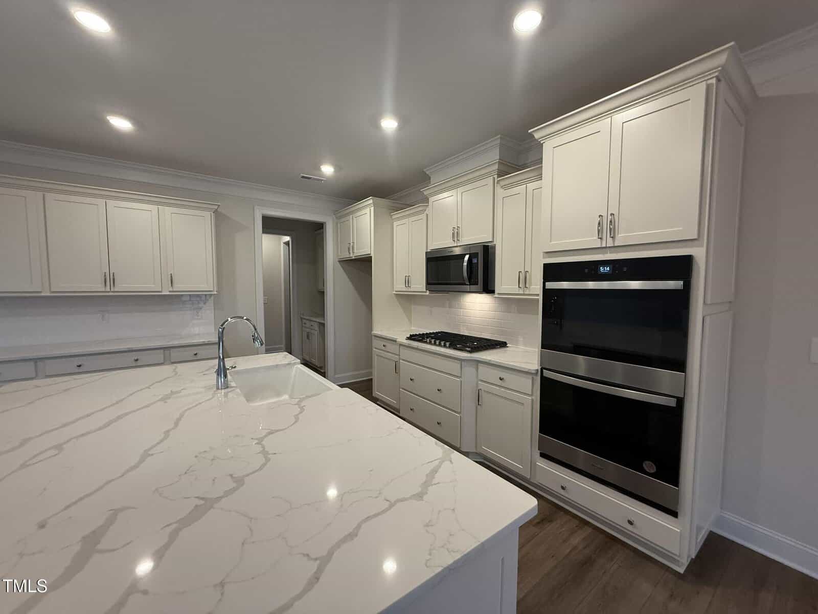 Spacious modern kitchen with white cabinets, stainless steel appliances, built-in oven and microwave, gas cooktop, and a large marble island with a sink under recessed ceiling lights.