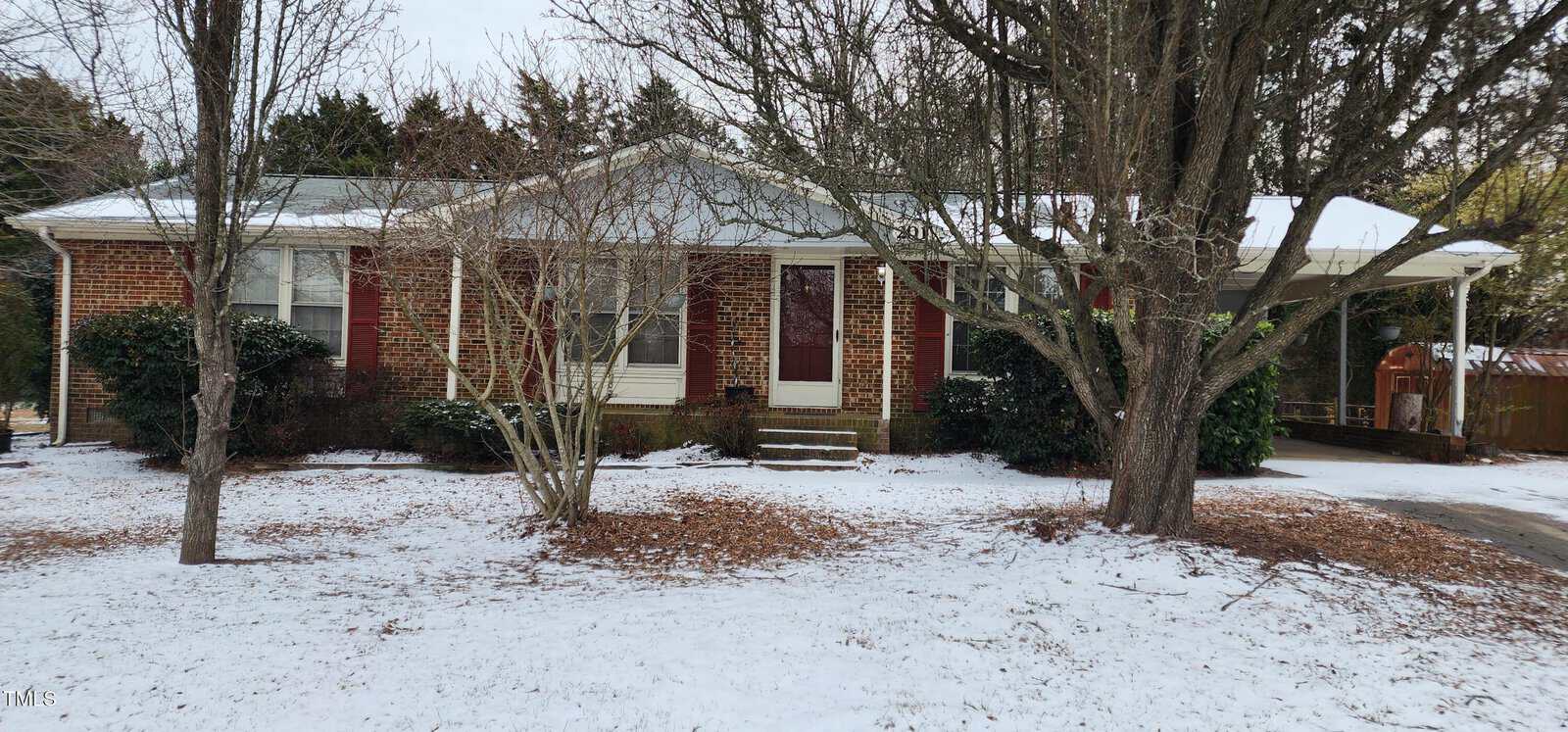 The brick house at 201 Providence Road, Oxford, with white-trimmed windows and a covered carport, is surrounded by bare trees on a snowy day. Steps lead to the front entrance, and patches of snow cover the driveway and ground.