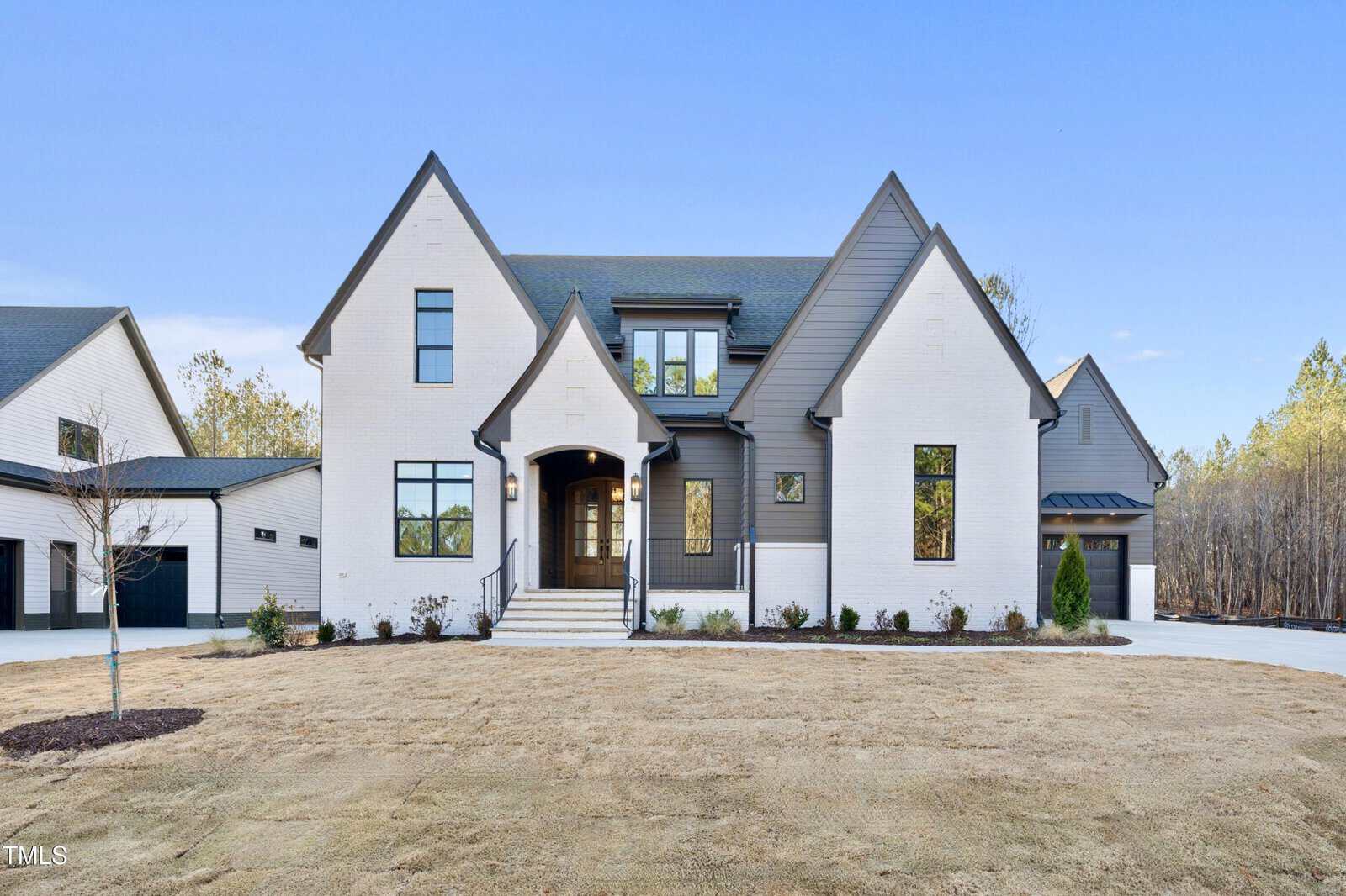 A modern two-story house with white brick and dark gray siding, featuring multiple large windows, a front porch with steps, and an attached garage. The front yard has minimal landscaping and a newly seeded lawn.
