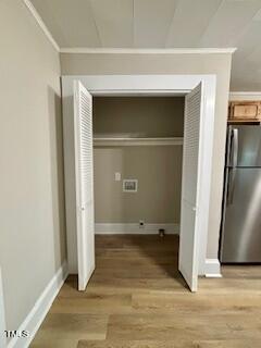White double doors open to reveal a small closet with light wooden flooring. Inside, there is a horizontal shelf near the top and an electrical outlet on the back wall. A portion of a stainless steel refrigerator is visible to the right.