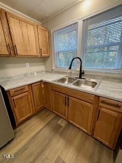 A kitchen corner with wooden cabinets and drawers, featuring a dual stainless steel sink with a black faucet. The countertop is marble-patterned, and there are two windows with blinds above the sink. The floor has wood-like tiles.