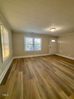 An empty room with light wood flooring and beige walls. There are two windows with partial blinds on the left and center, and a white door with a small window on the right side. A ceiling light fixture is present.