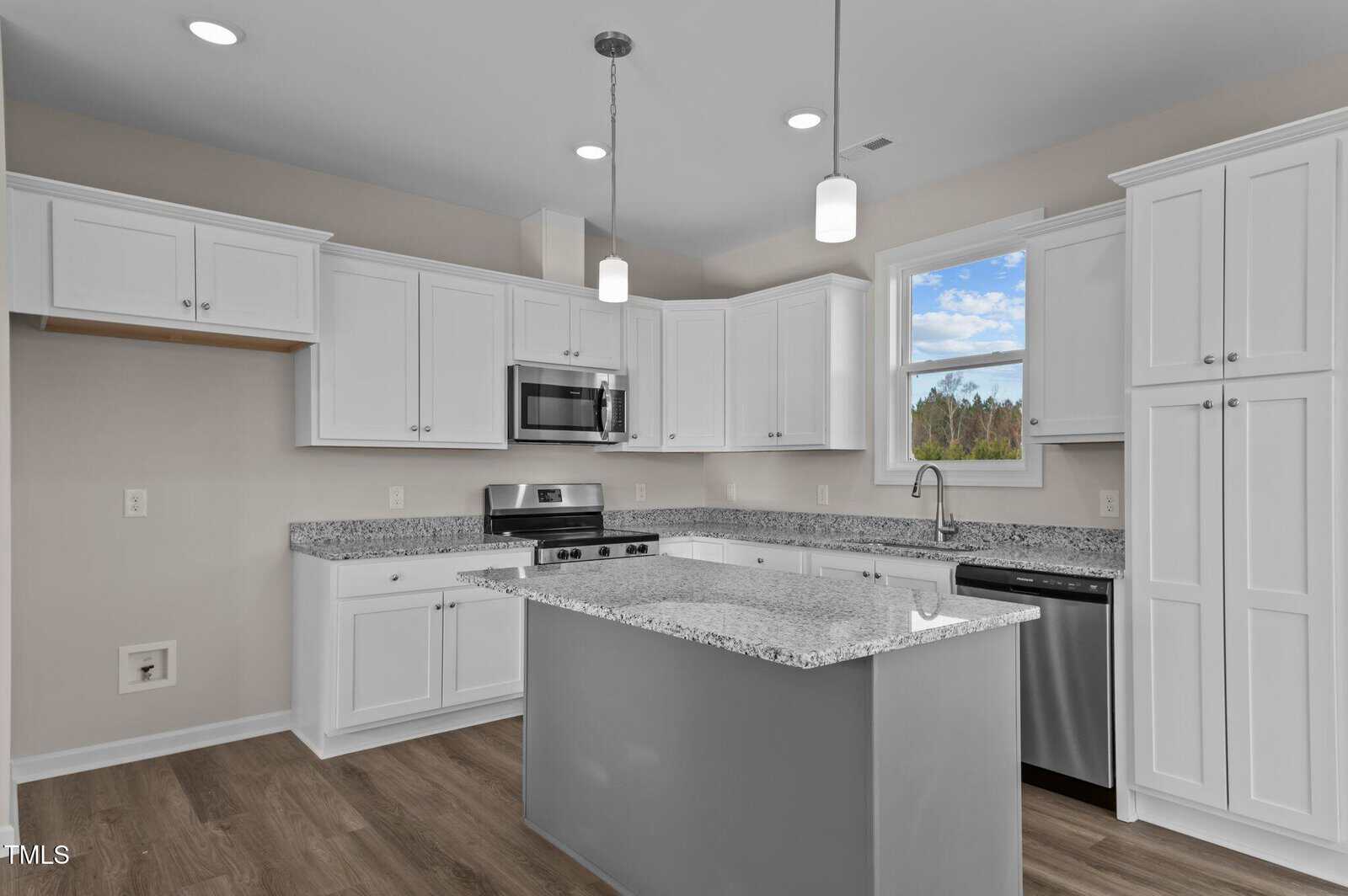 Modern kitchen with white cabinets, stainless steel appliances, granite countertops, a center island, wood flooring, and two pendant lights. A large window above the sink lets in natural light.