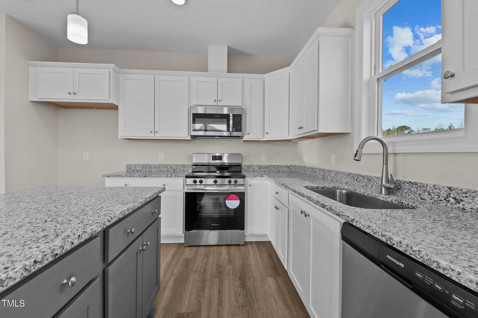 Modern kitchen with white cabinets, granite countertops, stainless steel appliances including a gas stove and microwave, a double sink under a window, gray lower cabinets, and wood-look flooring.
