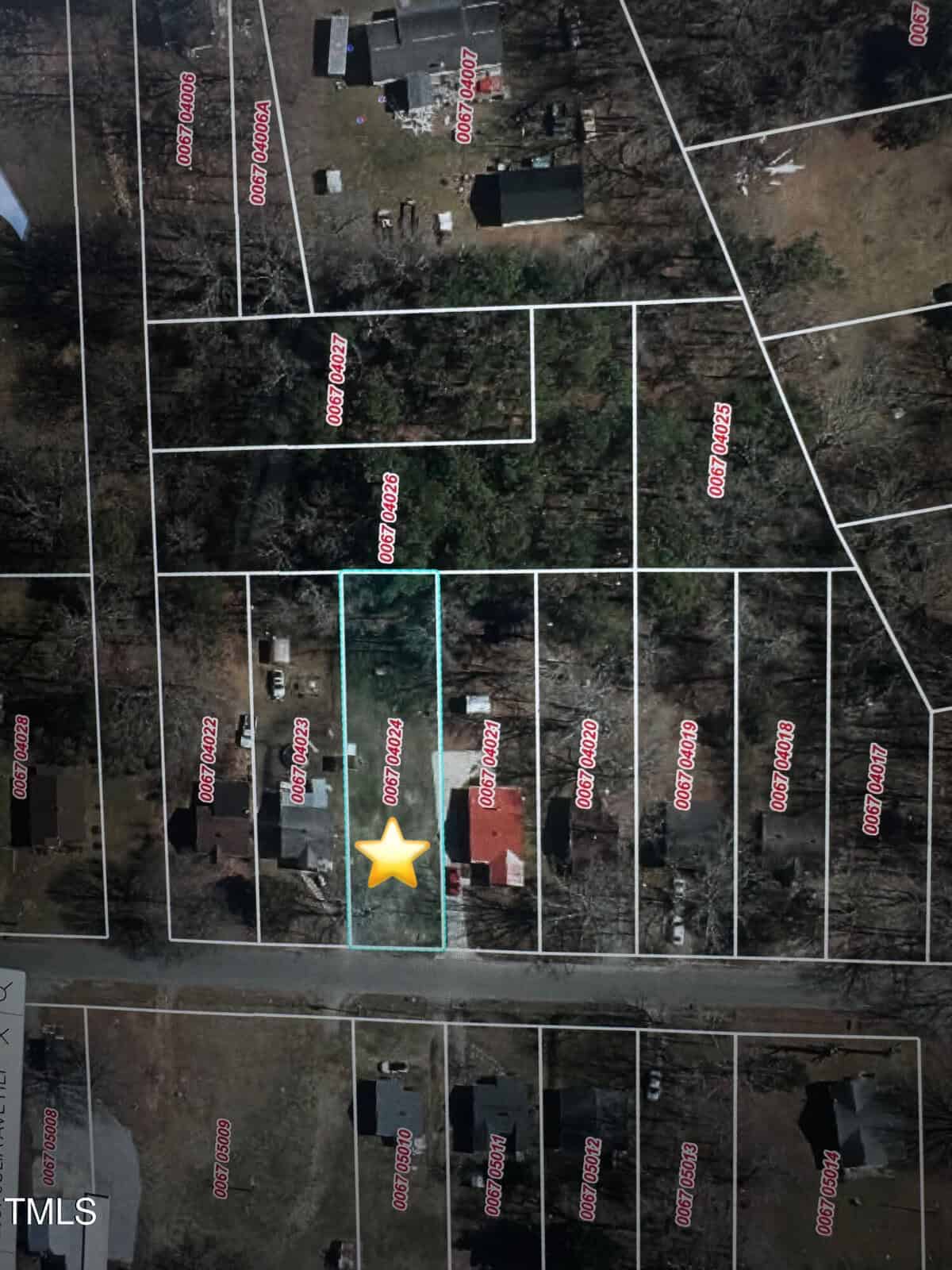 Aerial view of a residential area showing multiple rectangular plots marked with red numbers. A yellow star highlights one plot featuring a red-roofed house. Surrounding areas have trees, additional homes, and roads.