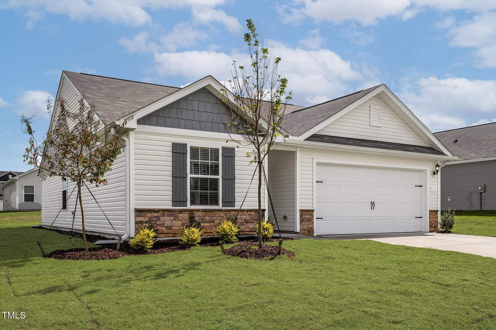 Located at 104 Shelfit Trail in Oxford, this single-story suburban house features white siding, a gray shingled roof, and charming stone accents. It boasts a two-car garage, landscaped yard with young trees and shrubs, and a welcoming driveway under a partly cloudy sky.