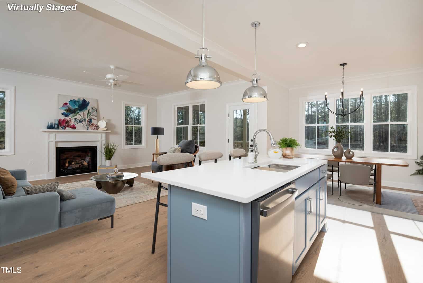 Bright, virtually staged open-concept living room and kitchen with a blue island, modern dining area, large windows, and a cozy fireplace, featuring contemporary furniture and decor.