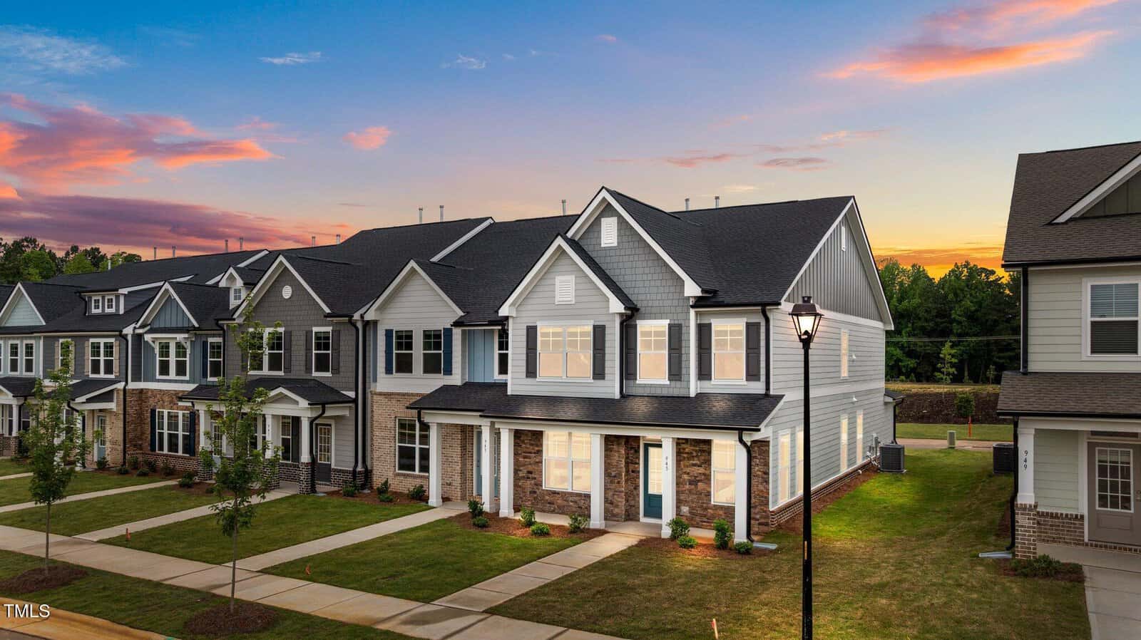 Row of modern two-story townhomes with gray and white exteriors, manicured lawns, and a sunset sky in the background; a streetlamp stands near the sidewalk in front at 945 Alma Railway Drive in Wake Forest.
