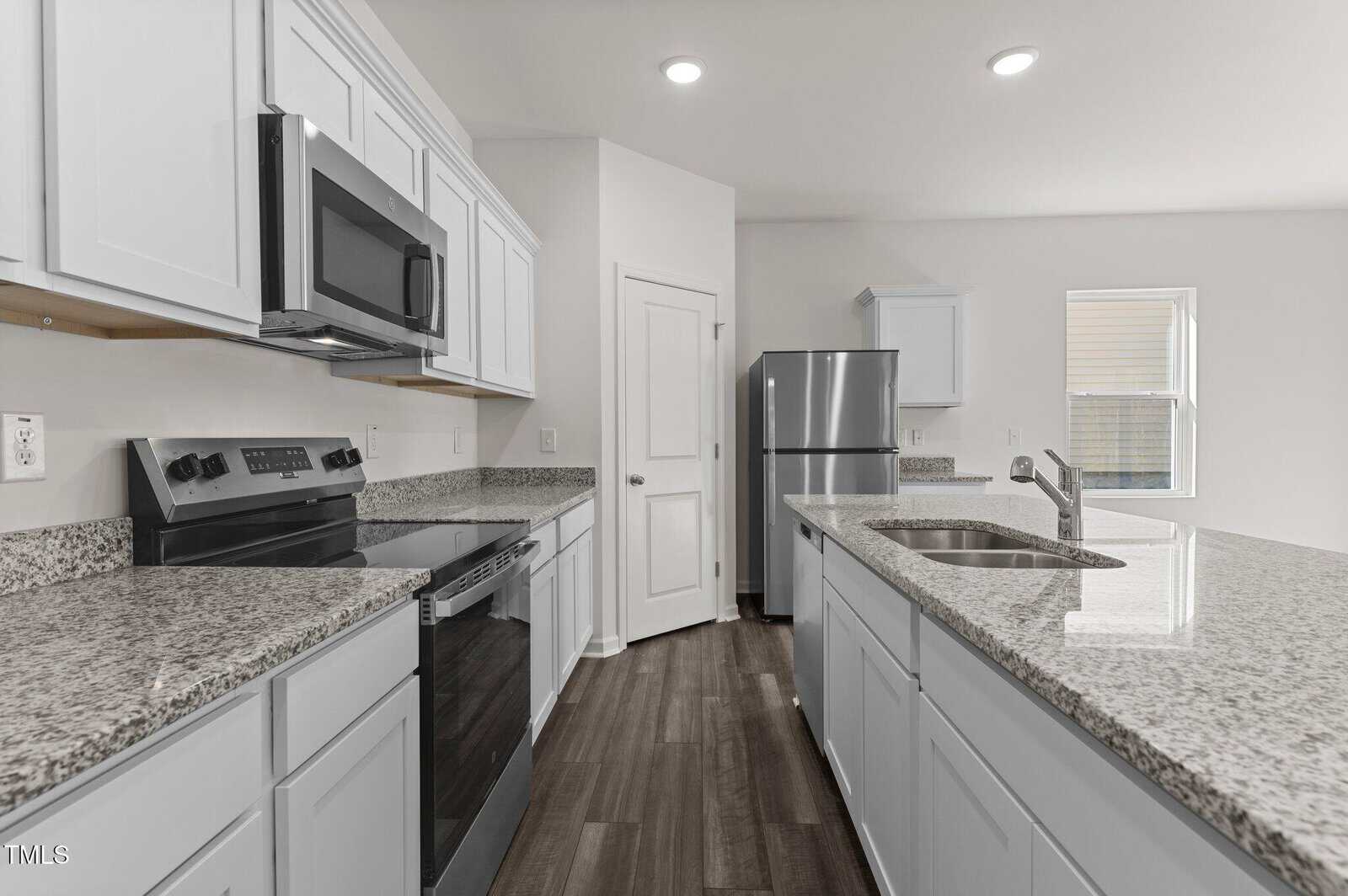 A modern kitchen with white cabinets, stainless steel appliances, granite countertops, a central island with a sink, and wood-style flooring. There is a window bringing in natural light.
