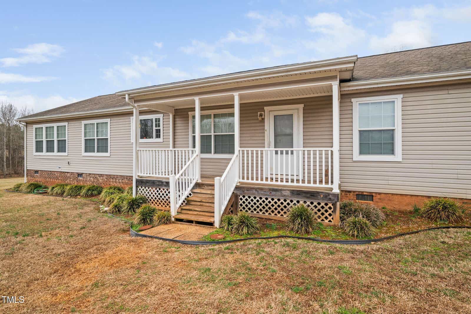 This charming single-story house at 6001 Rock Bottom Road, Oxford, boasts gray siding and a quaint porch with white railings. The grassy yard is adorned with shrubs lining the foundation, while the gabled roof and numerous front windows complete its inviting appeal.