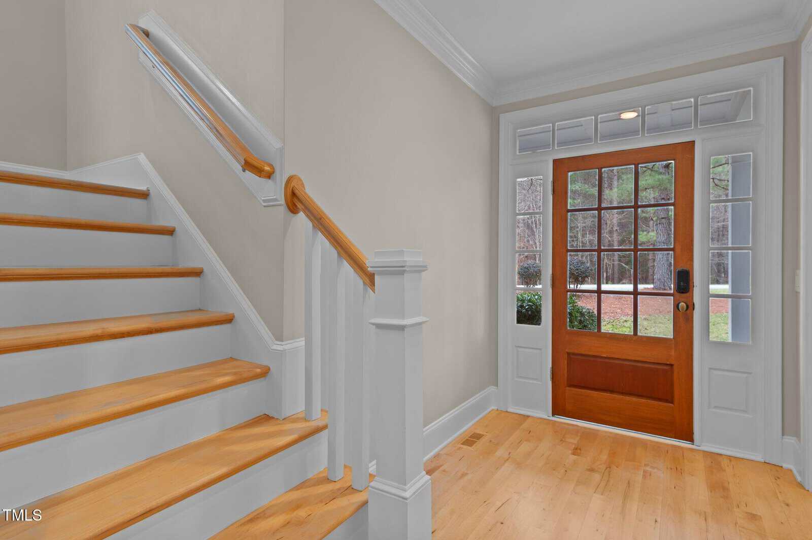 Entryway with light wood floors, a wooden front door with glass panels, sidelight windows, beige walls, white trim, and a staircase with wooden steps and white risers leading to the upper floor.