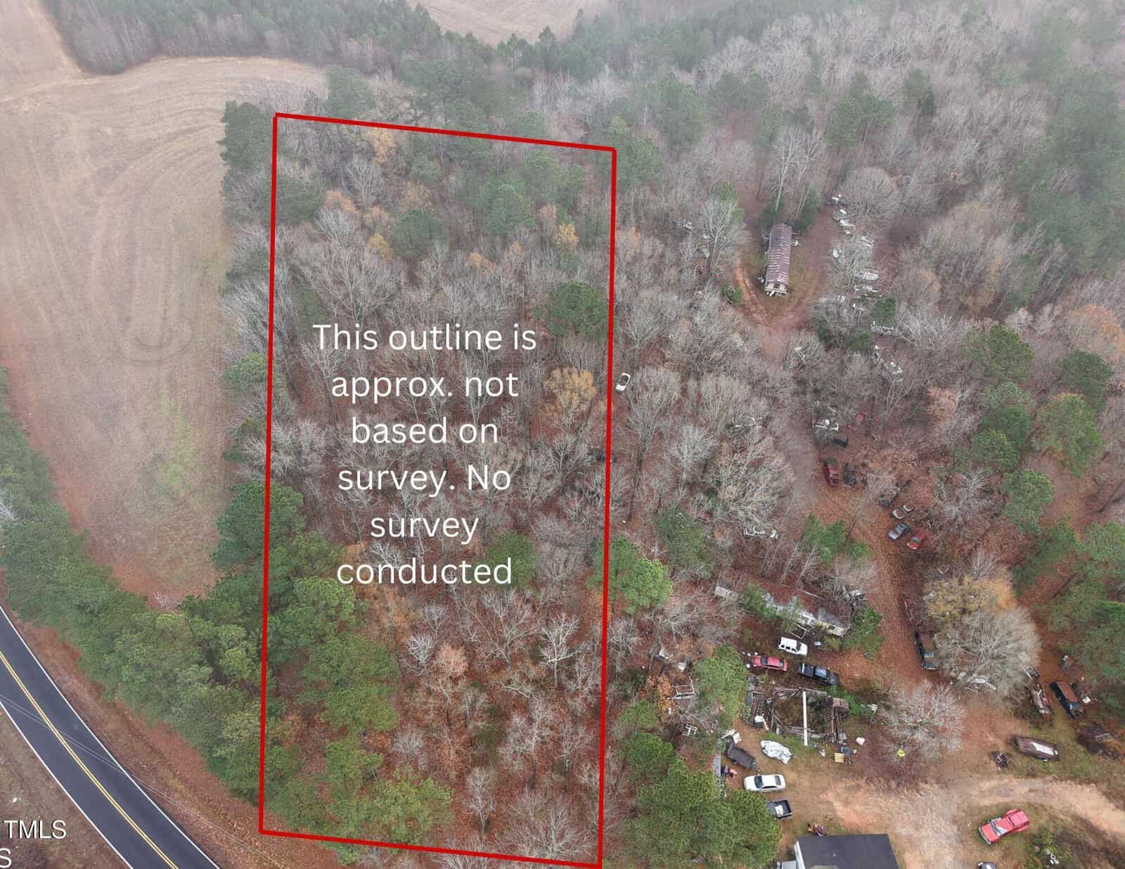 Aerial view of a wooded area bordered by a red rectangle labeled “This outline is approx. not based on survey. No survey conducted.” Nearby are a curved road, parked vehicles, and some buildings surrounded by trees.