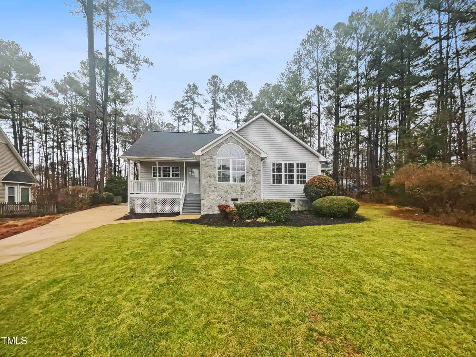 Nestled on 1419 Mangum Avenue in Creedmoor, this single-story house boasts a well-maintained yard with a concrete driveway. It features a blend of stone and siding on the exterior, an arched window, and a cozy front porch surrounded by trees and shrubs under the clear blue sky.