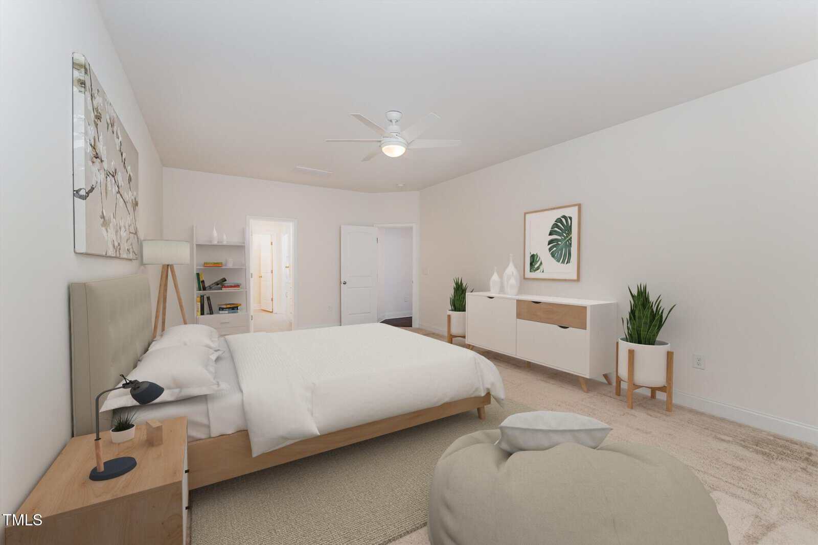A bedroom with a bed, two nightstands, a sideboard, plants, a ceiling fan, and neutral decor. The walls are white, and there is beige carpet on the floor. A doorway leads to another room.