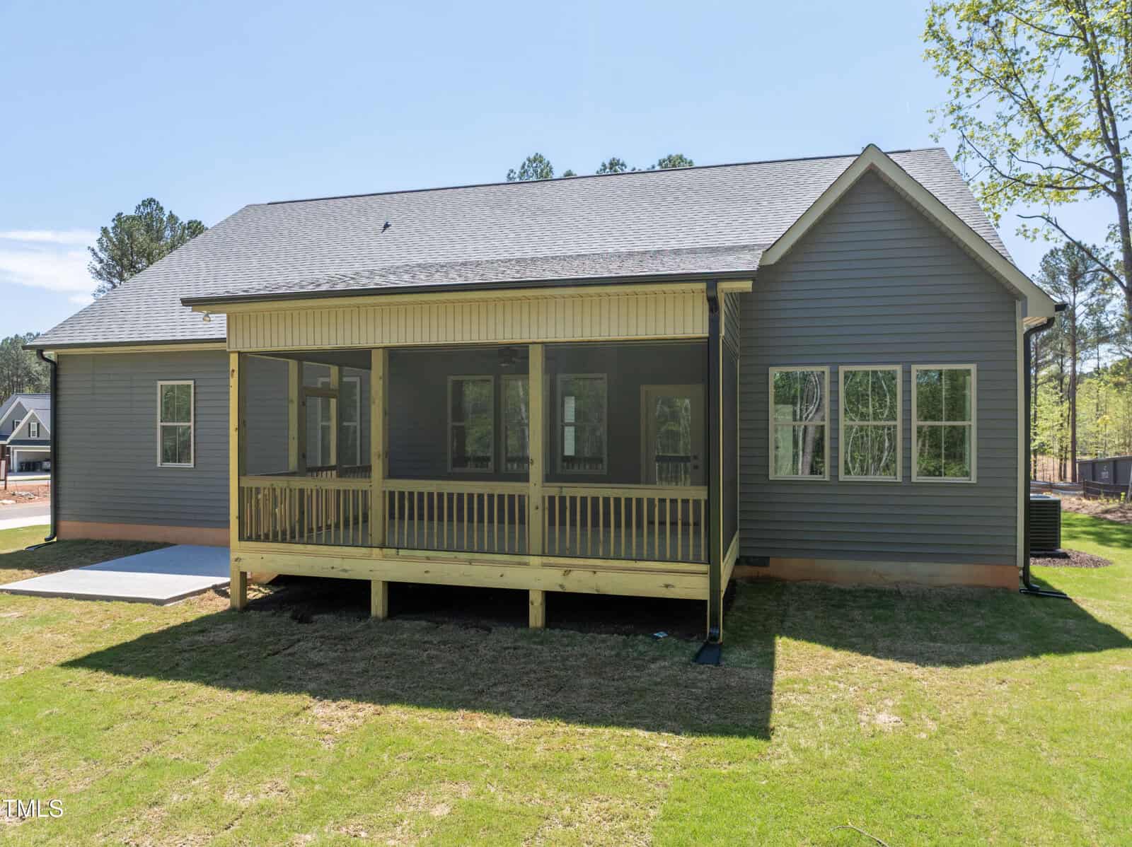 A single-story house with gray siding, a gabled roof, and a screened-in back porch with wooden railings, overlooking a grassy backyard. Several windows are visible on the house.