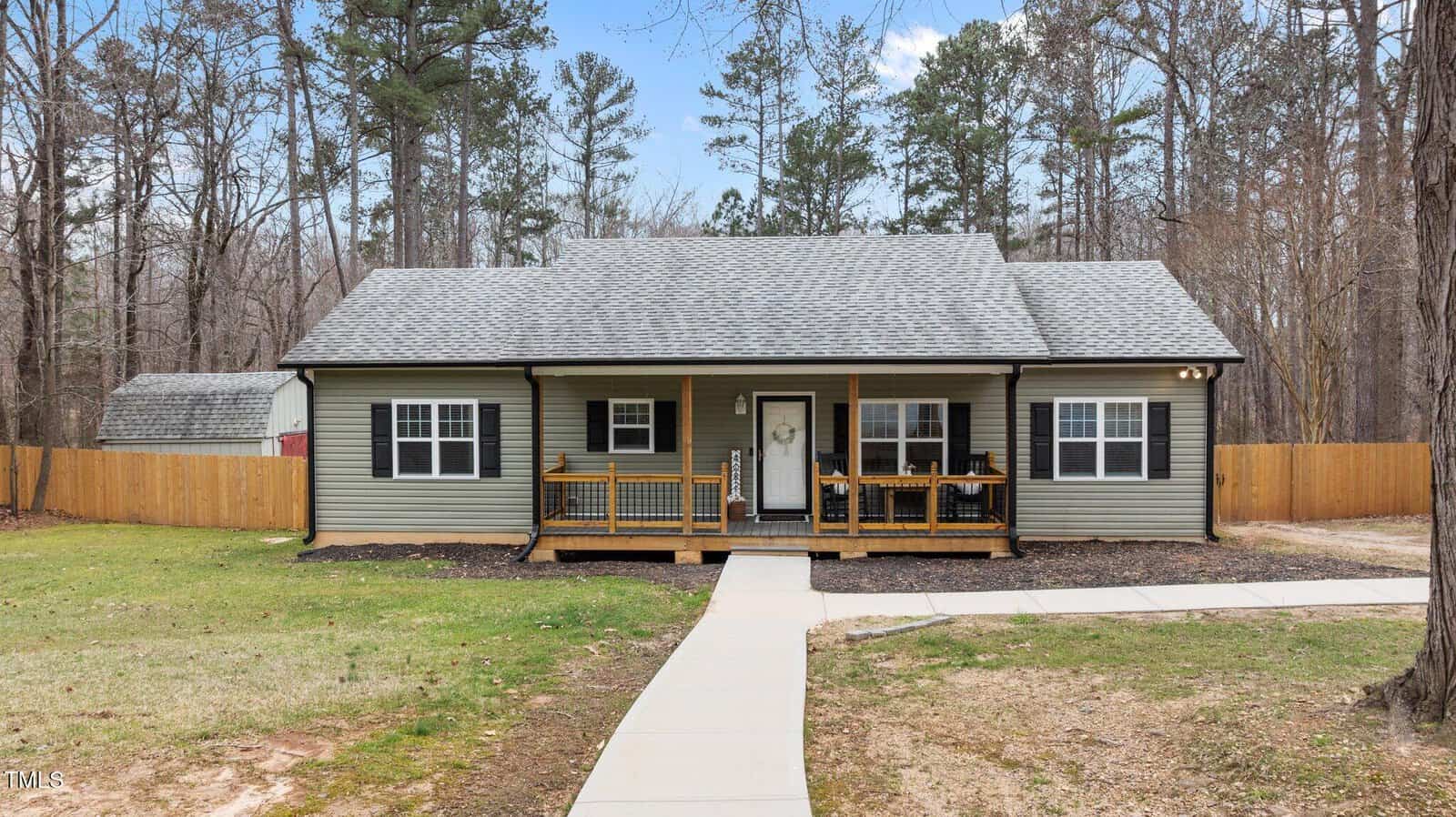 Nestled along 4082 Old Franklinton Road, this charming green, single-story house with a gray roof is embraced by trees. Featuring a wooden front porch adorned with a wreath and a pathway leading to it, the property in Franklinton includes a fenced yard and a shed in the background.