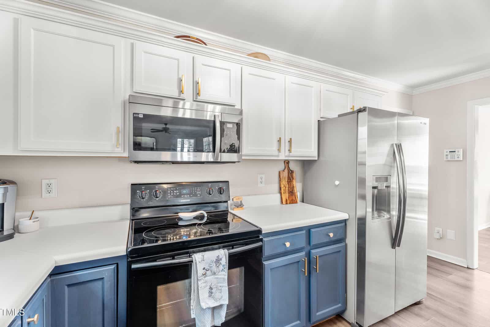 Modern kitchen with blue lower cabinets and white upper cabinets, stainless steel appliances including a stove, microwave, and refrigerator, white countertops, and wooden cutting boards on top of the cabinets.