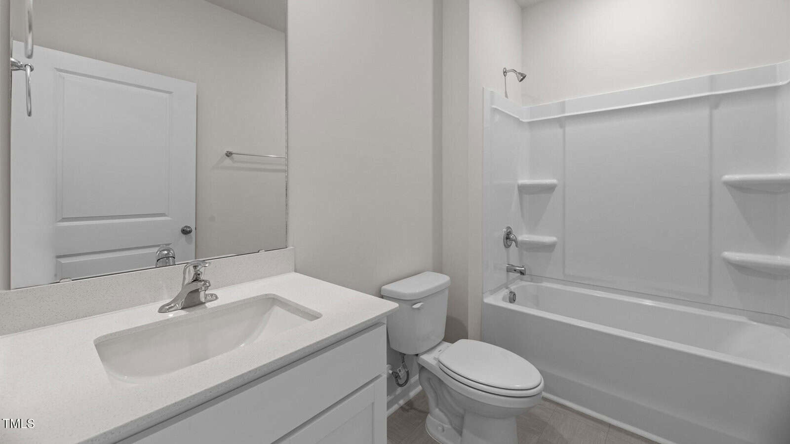 A clean, modern bathroom with a white sink vanity, a toilet, a towel rack, and a white bathtub with built-in shelves. The walls and door are light-colored, and lighting is bright.