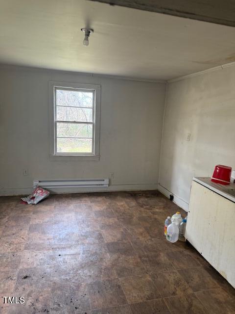 A small, empty room with a single window and a bare light bulb on the ceiling. The floor is covered with patterned vinyl tiles. A few items, including plastic jugs and a red container, rest on a white countertop to the right.