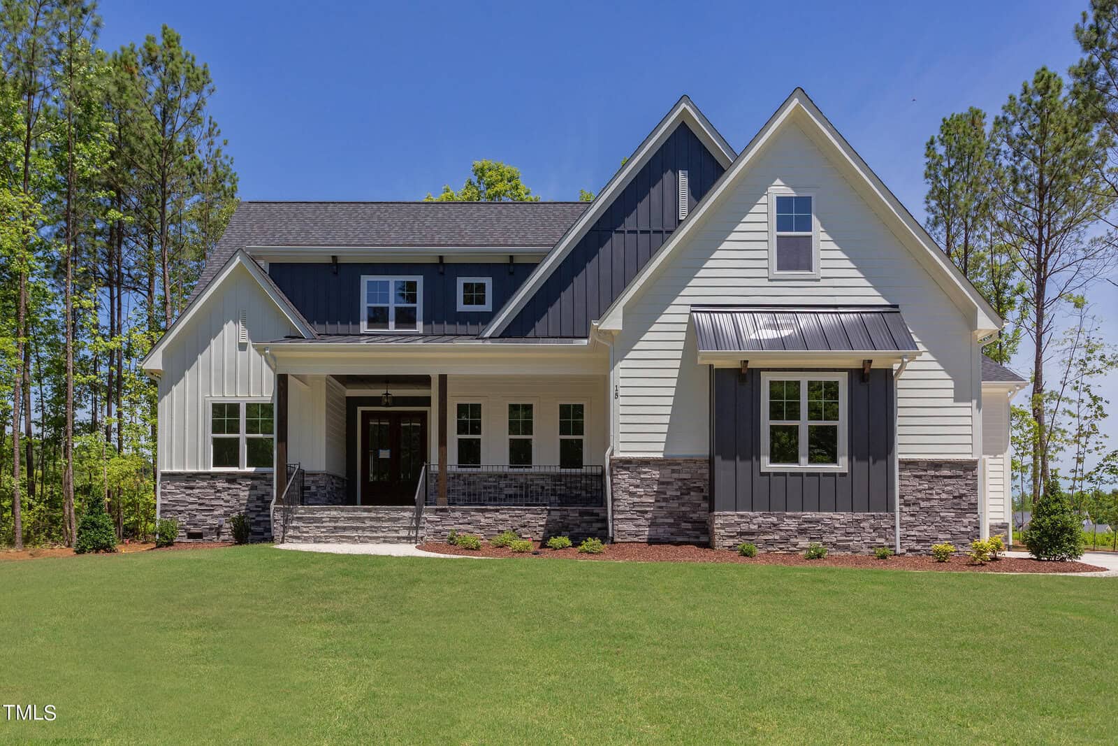 A modern two-story house at 15 Harvest View Way in Franklinton, featuring gray and white siding, stone accents, a covered front porch, large windows, and a well-maintained green lawn surrounded by tall trees.