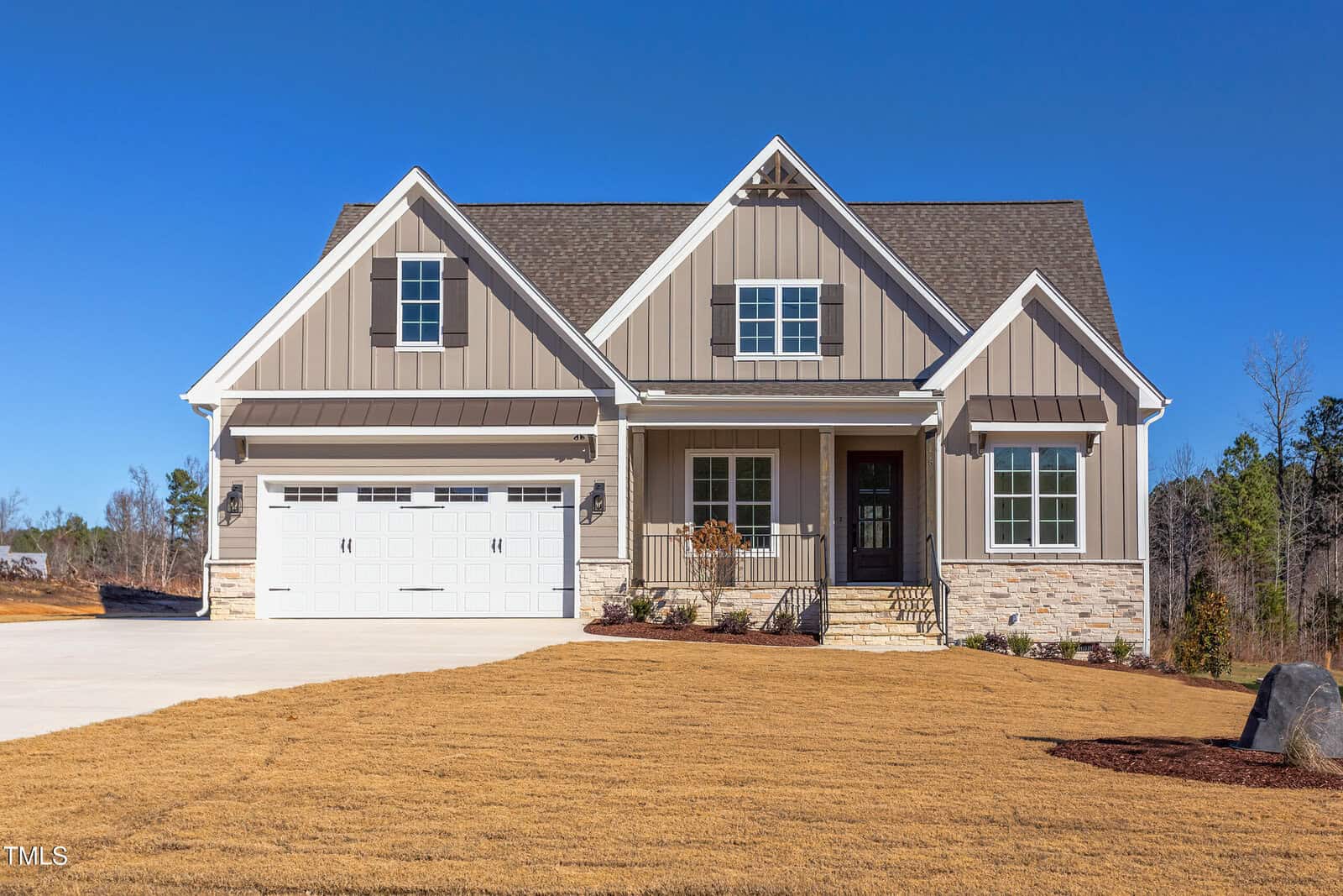 A modern beige house with white trim, a double garage, front porch, and gabled roof sits on a large lawn under a clear blue sky with trees in the background at 75 Harvest View Way in Franklinton.