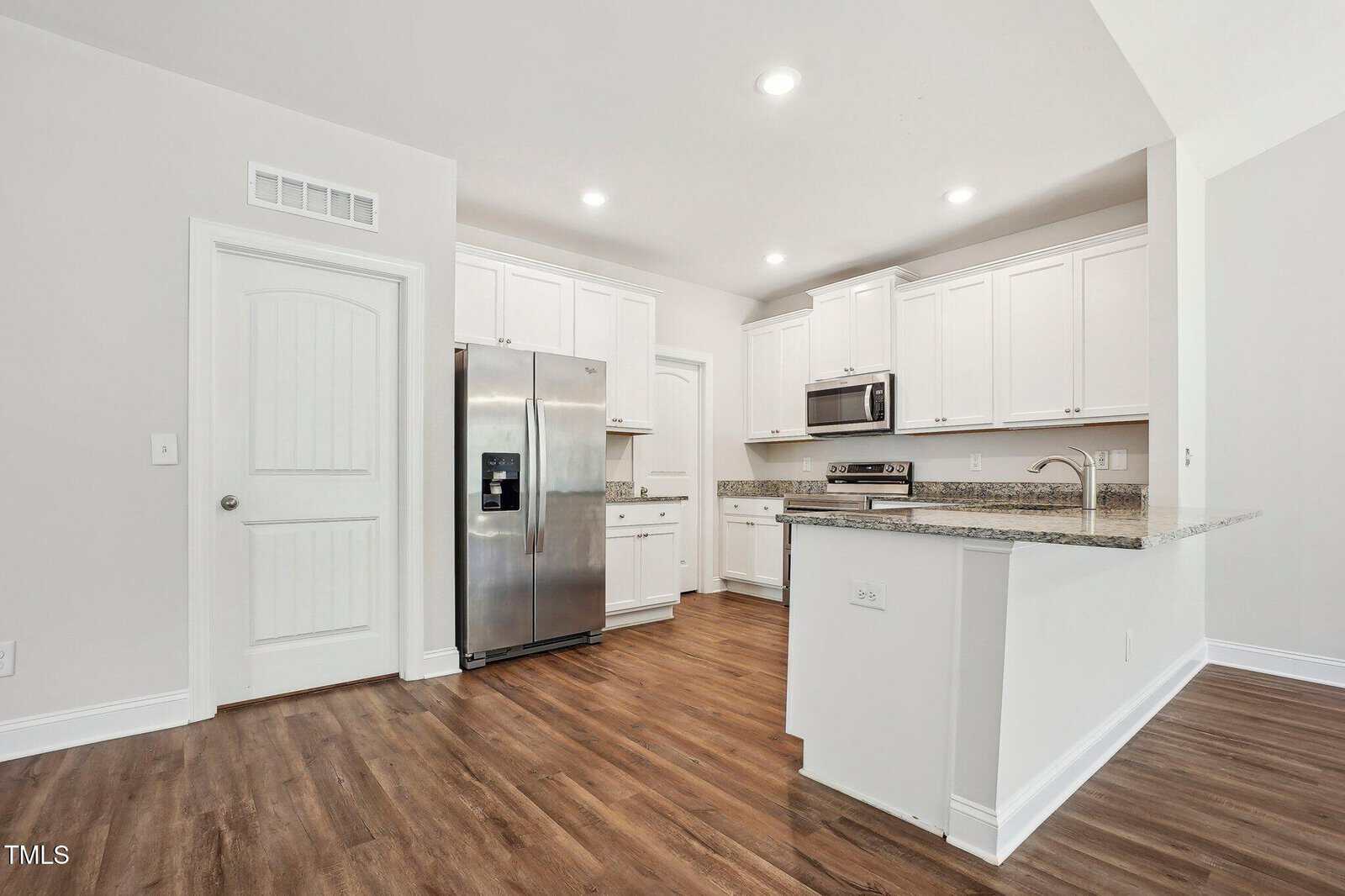 Modern kitchen with white cabinets, stainless steel appliances, granite countertops, a large refrigerator, microwave, dishwasher, and wood flooring. Recessed lighting and a peninsula with an overhang for seating.