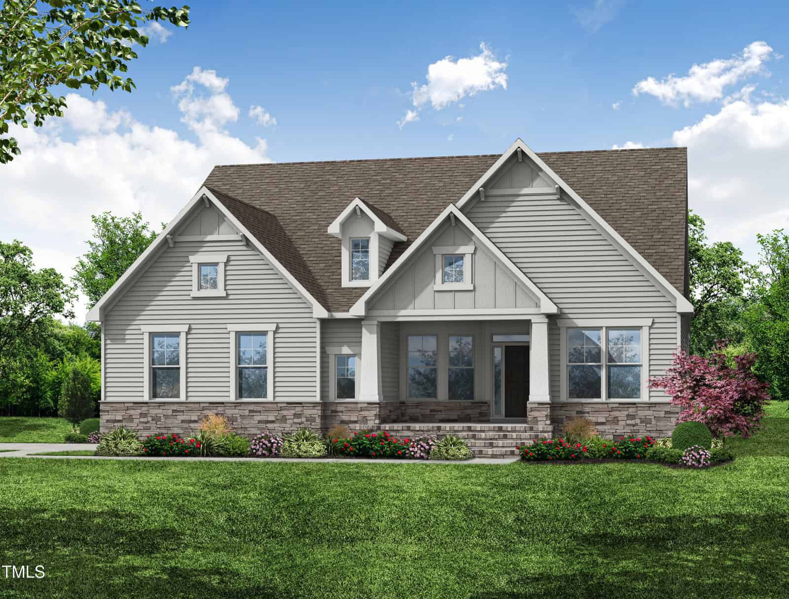 A two-story house with gray siding, a brown gable roof, front porch with columns, stone foundation, and landscaped front yard with green grass, shrubs, and blooming flowers under a partly cloudy sky.