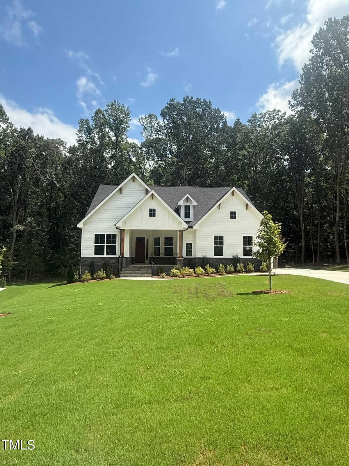 A modern two-story white house with dark roofing and a front porch sits on a large, neatly mowed lawn at 60 Valebrook Court in Youngsville, surrounded by trees under a blue sky with scattered clouds.