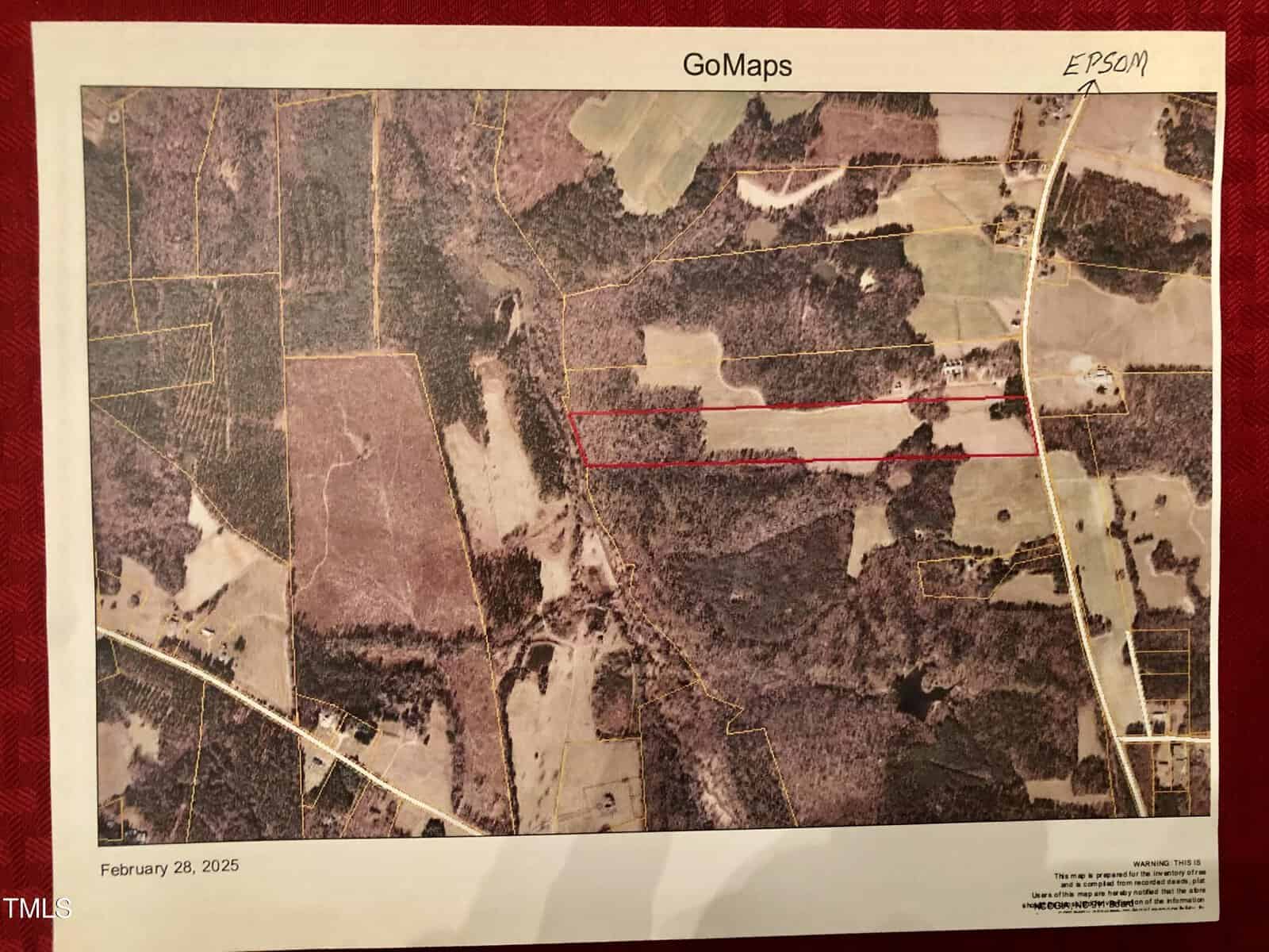 A printed satellite map titled "GoMaps," dated February 28, 2025, showing a rural area with fields, wooded sections, and roads. A red line demarcates a specific area on the map. Additional handwritten notes appear in the top right corner.