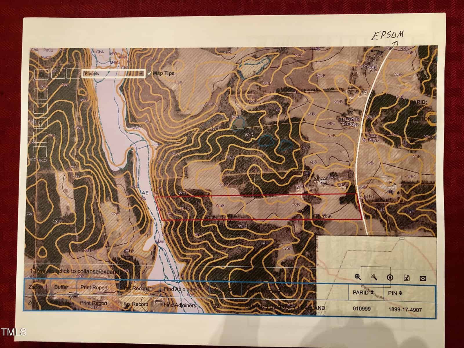 A topographical map featuring contour lines showing elevation changes. It includes a river on the left, various labeled plots, a highway on the right, and an area enclosed in red. Labels and coordinate details are visible on the document.