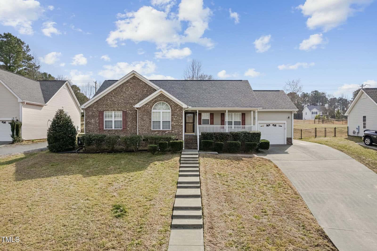 Located at 2574 Primrose Lane, this charming single-story brick house in Creedmoor boasts an arched window and a covered porch. A concrete walkway and driveway lead to the attached garage. The sky is partly cloudy, with neighboring houses visible on either side.