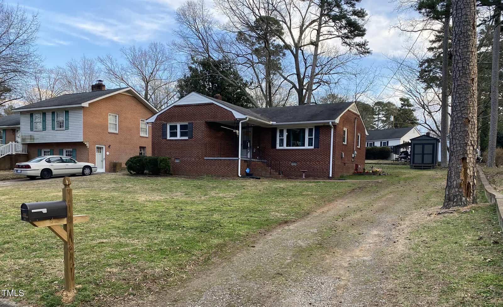 A charming single-story brick house at 103 W Thorndale Drive with a front porch overlooks a yard with a grass driveway. A black mailbox on a wooden post stands proudly, while trees and neighboring homes frame this Oxford gem in the background.