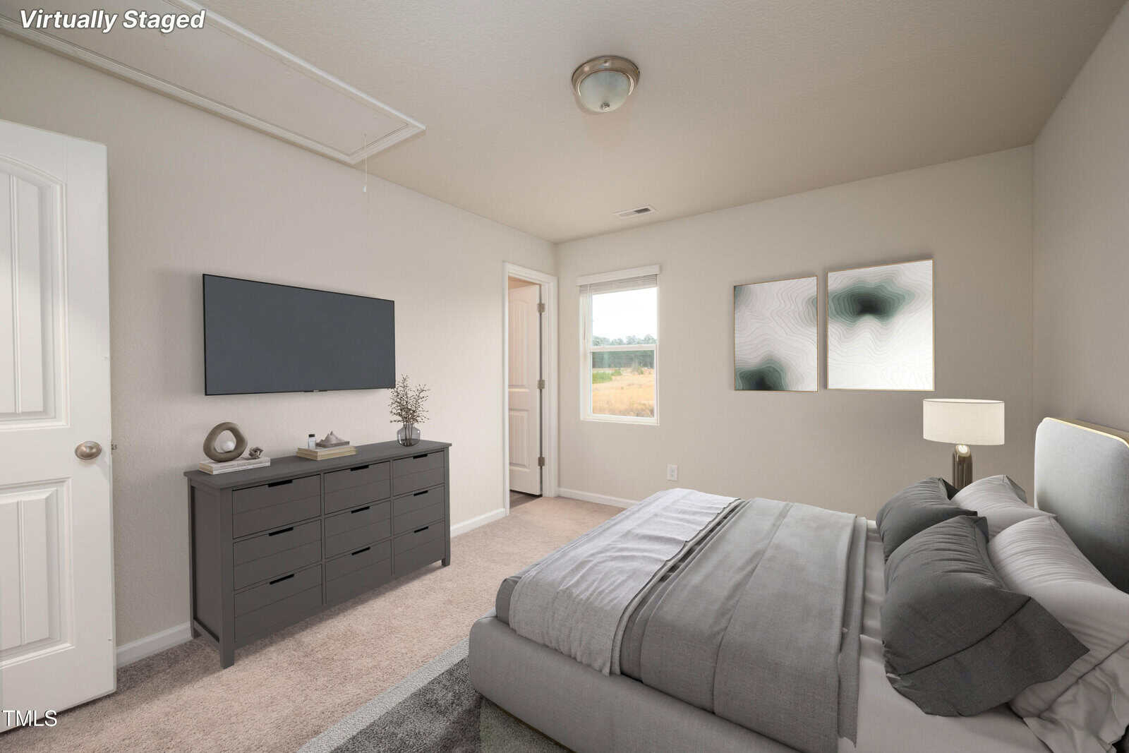 Bedroom with neutral walls, a bed with gray bedding, a gray dresser with decor, wall-mounted TV, two abstract art pieces, a lamp, window, and open door. The room is virtually staged and has carpet flooring.