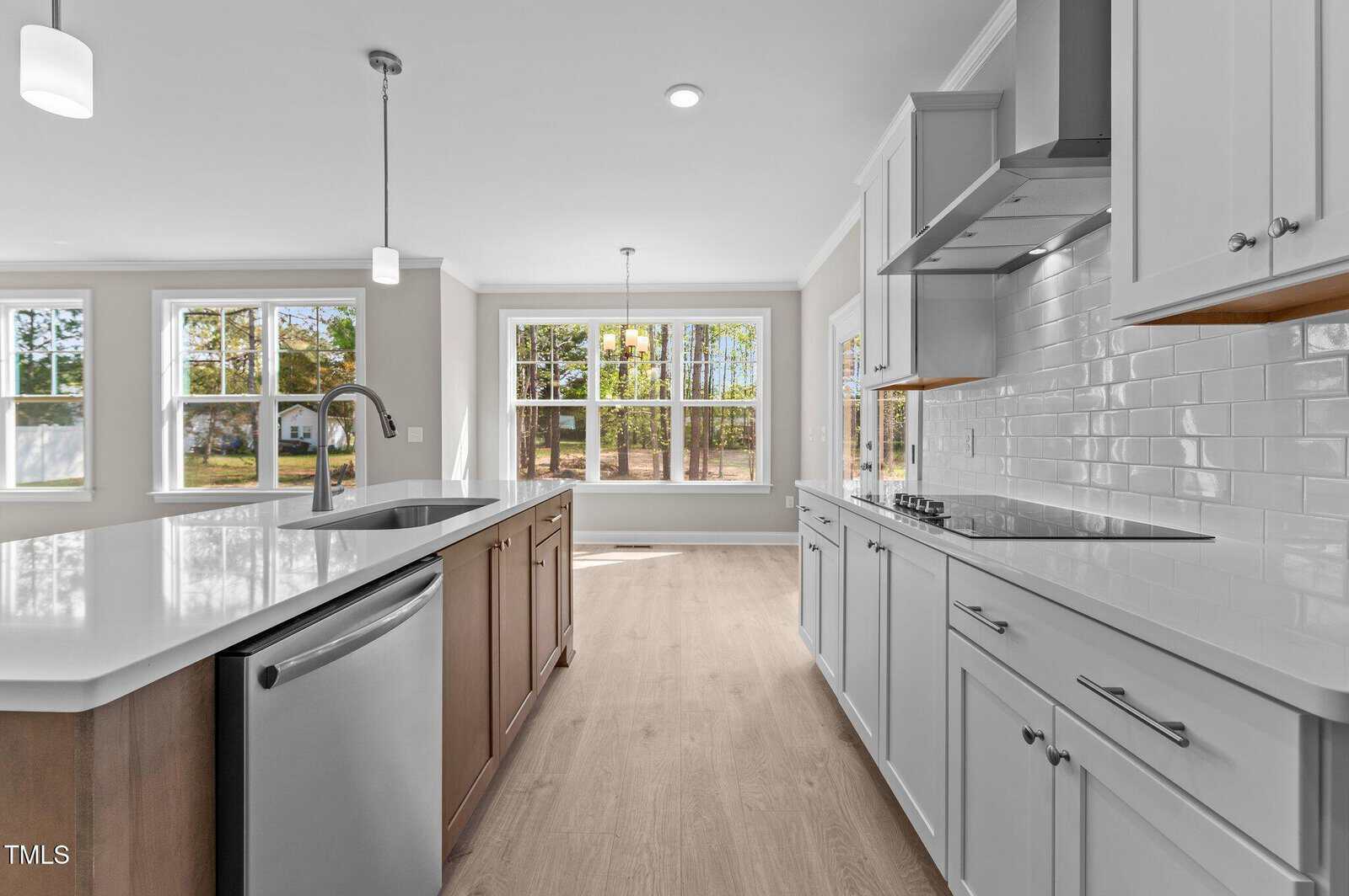 Modern kitchen with white cabinets, a large island featuring a built-in sink and dishwasher, stainless steel appliances, and bright windows letting in natural light. Light wood flooring and white tile backsplash.