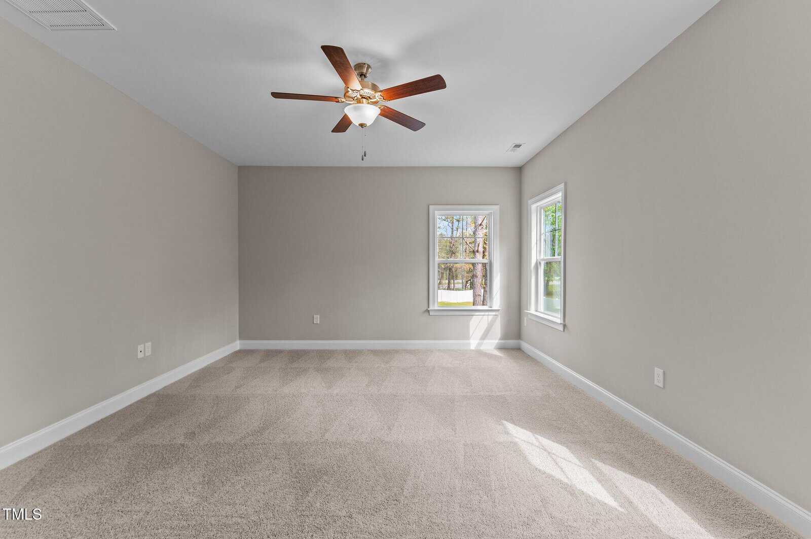 Empty room with beige walls and carpet, a ceiling fan with lights, and two windows letting in natural light.