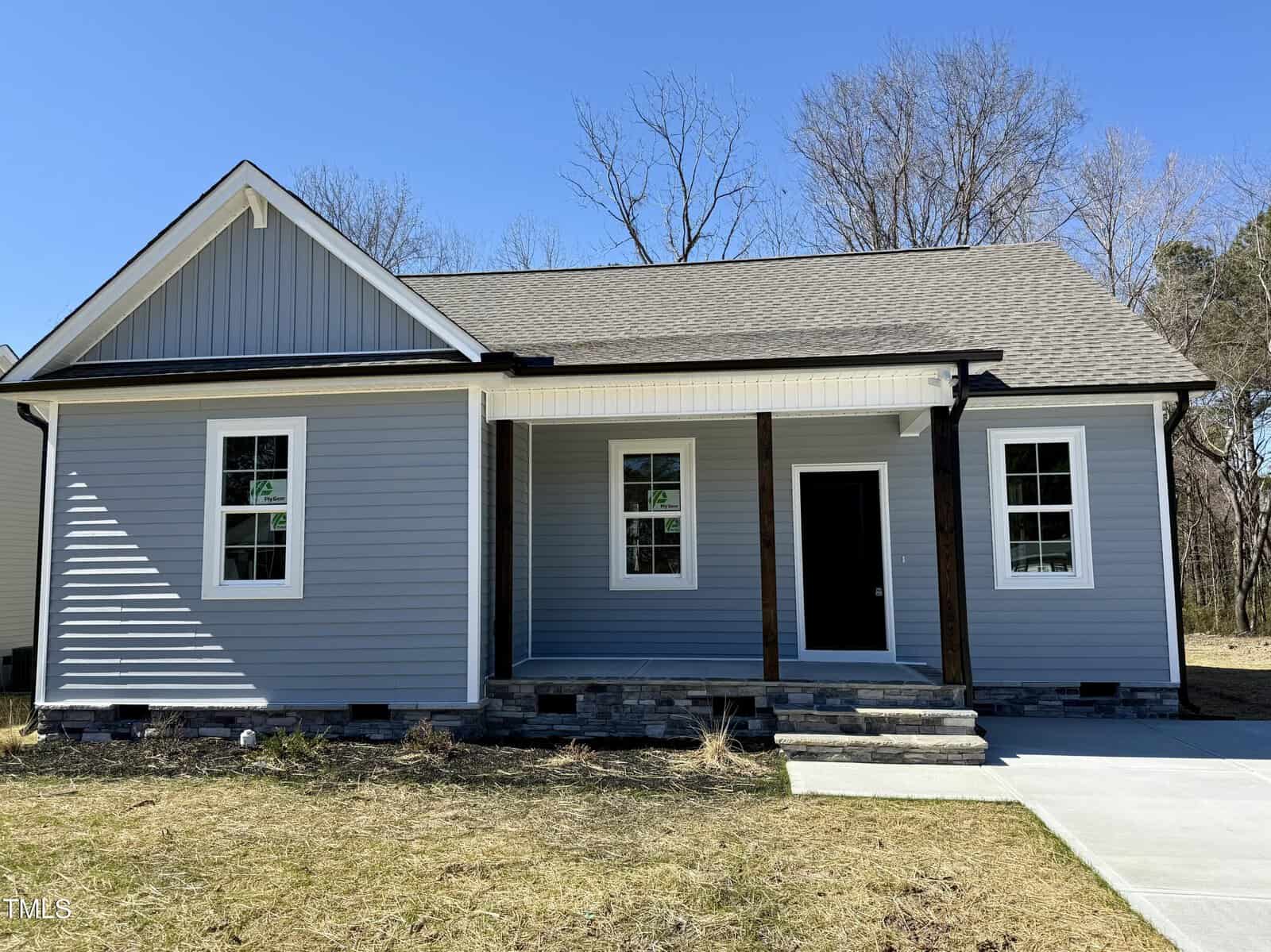 Nestled at 119 Daniel Street in Oxford, this single-story house features gray siding and a pitched roof. A cozy front porch, supported by wooden posts with stone accents, welcomes you. The facade is adorned with three windows and a concrete path that winds through the sparse grass yard.