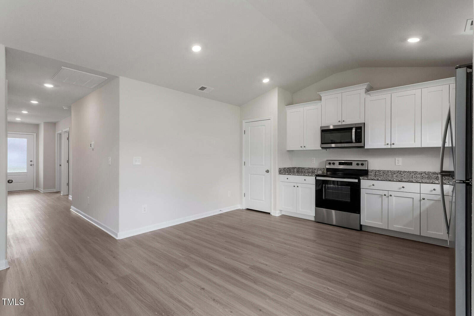 Modern kitchen with white cabinets, stainless steel appliances, granite countertops, and wood-look flooring. An open space layout with recessed lighting and a hallway leading to another part of the home. Walls are painted in a light neutral color.