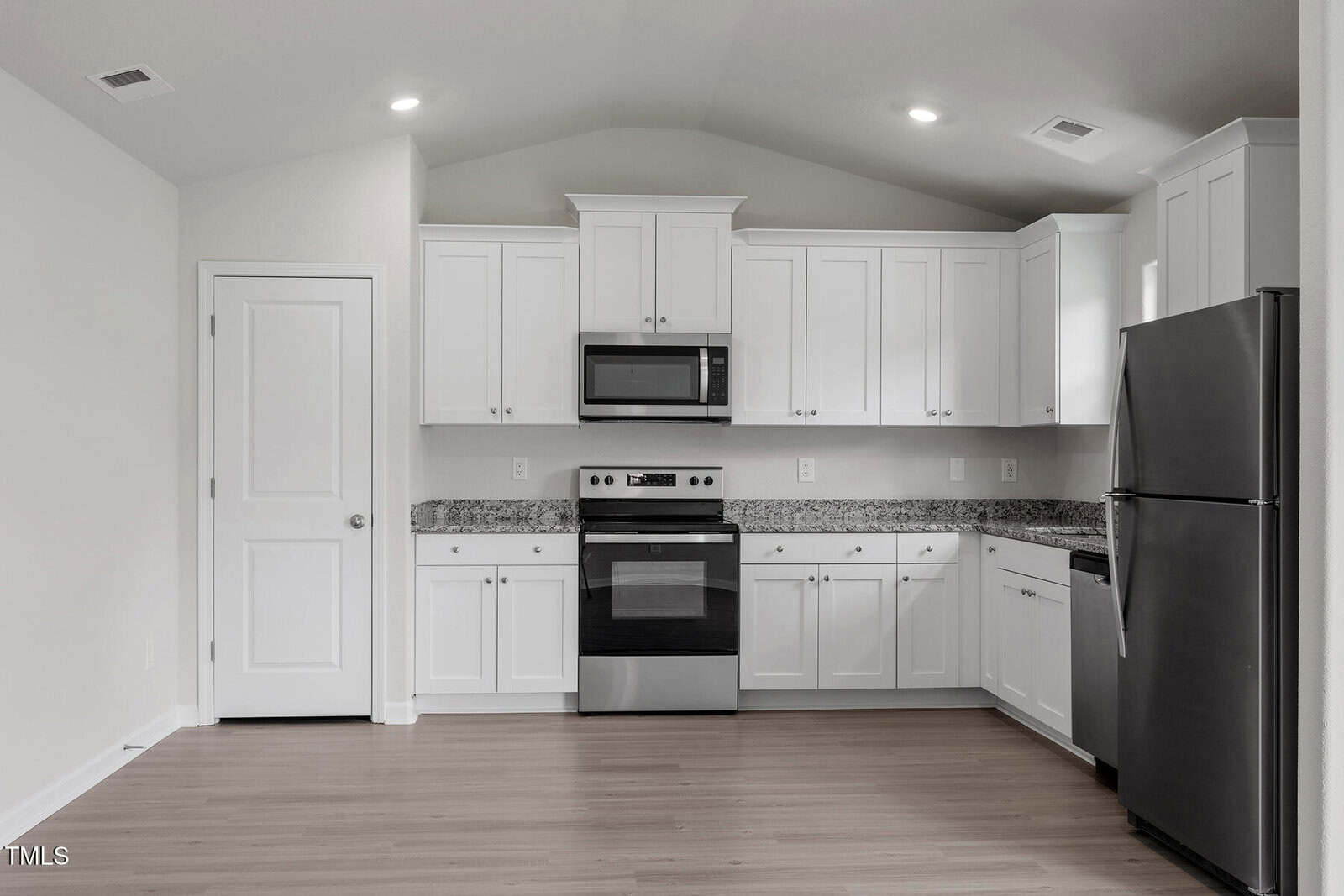 A modern kitchen with white cabinets, a microwave, stove, and a refrigerator. The countertop is granite, and the flooring is light wood. The ceiling has recessed lighting, and there is a closed door on the left side.