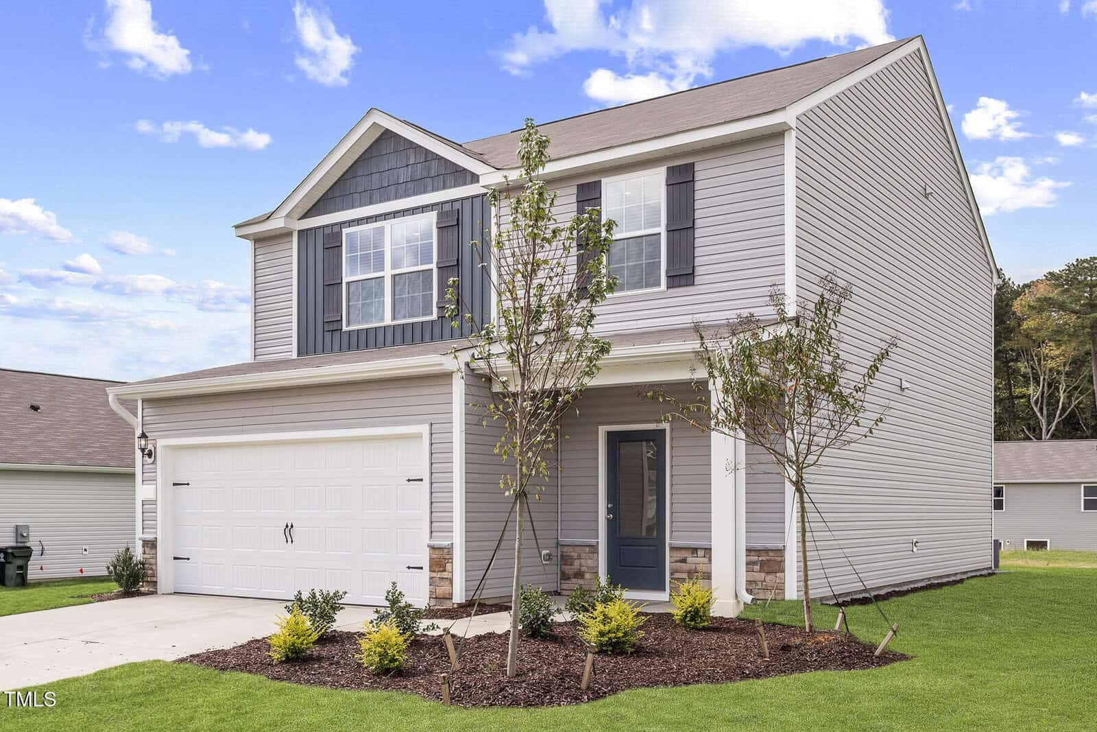 The two-story Oxford residence on 909 Rhino Bend boasts a modern design with gray siding, dark gray accents, and white trim. It features a welcoming front porch, a spacious two-car garage, and a landscaped yard adorned with small trees and shrubs under a partly cloudy sky.