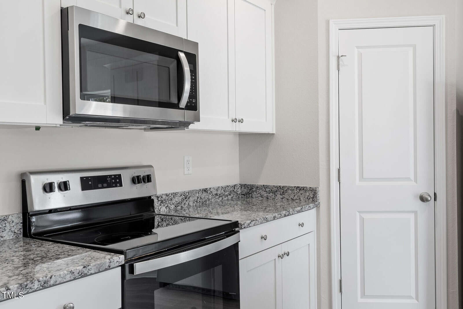 Modern kitchen with white cabinets, granite countertops, and stainless steel appliances, including a microwave and an electric stove with an oven. A white pantry door is on the right side of the image.