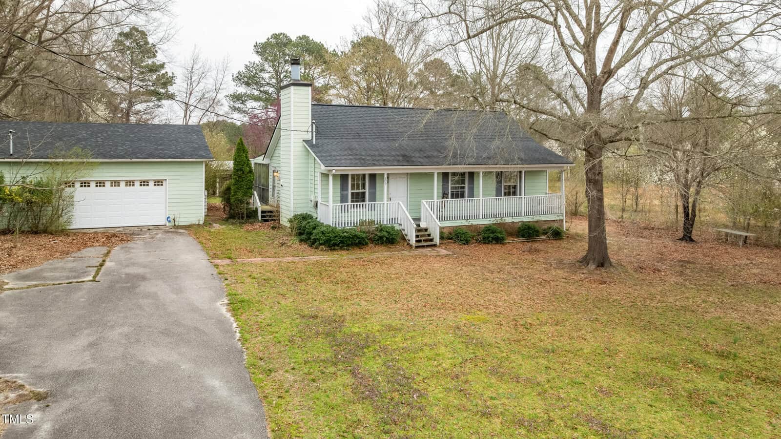 A light green single-story house with a front porch and chimney, set on a grassy lot with leafless trees at 879 Cheves Road, Zebulon. A detached two-car garage is to the left, and a paved driveway leads up to the house and garage.