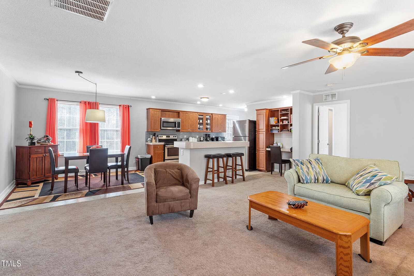 Open living space with a kitchen, dining area, and living room. Includes wooden cabinets, appliances, a dining table with four chairs, a sofa, armchair, coffee table, and ceiling fan. Neutral colors dominate the decor.