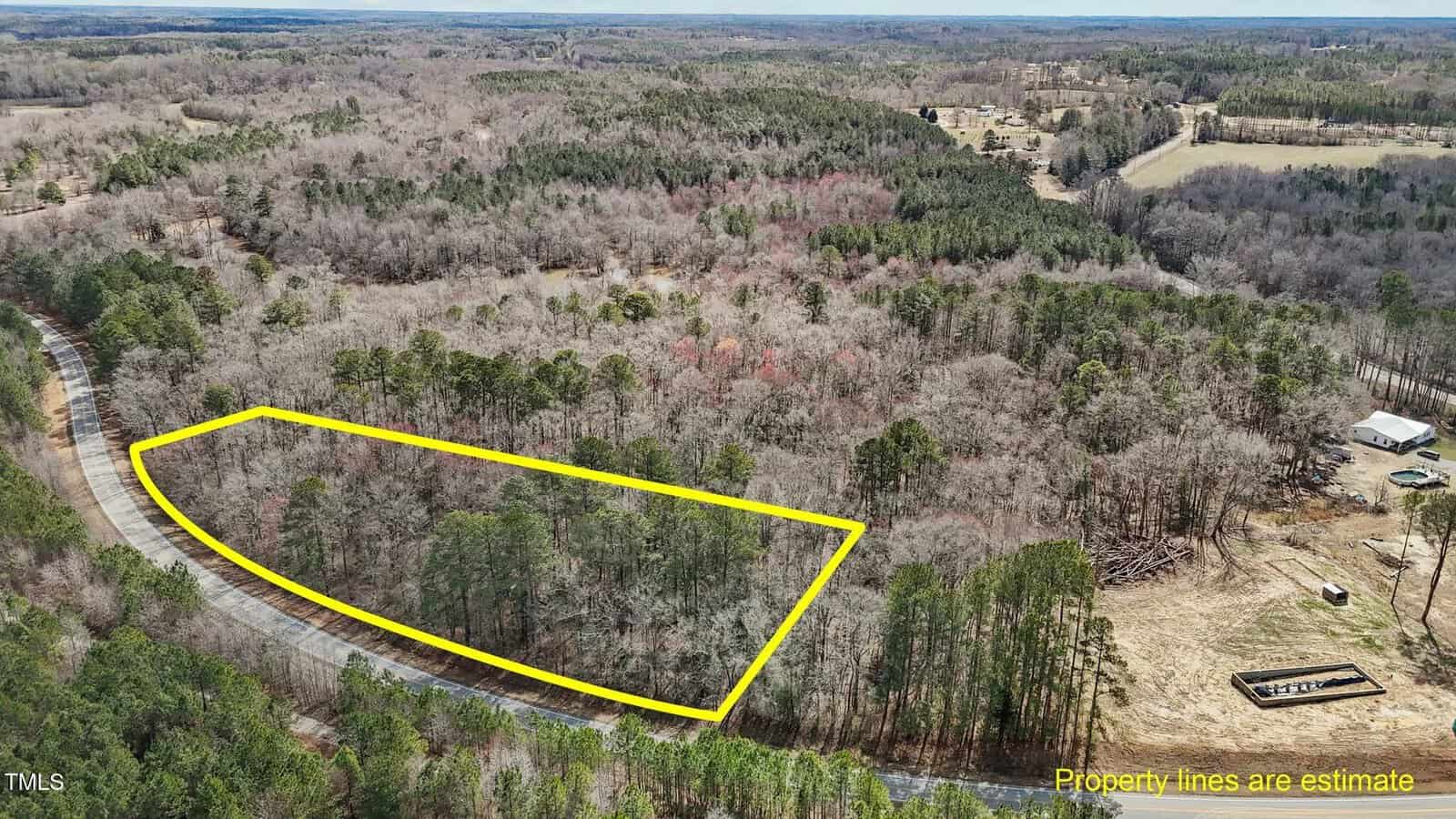 A wooded plot of land is outlined in yellow in a rural area with a curved road along one side. Surrounding areas feature dense trees, open clearings, and a few scattered structures. Text notes property lines are estimates.