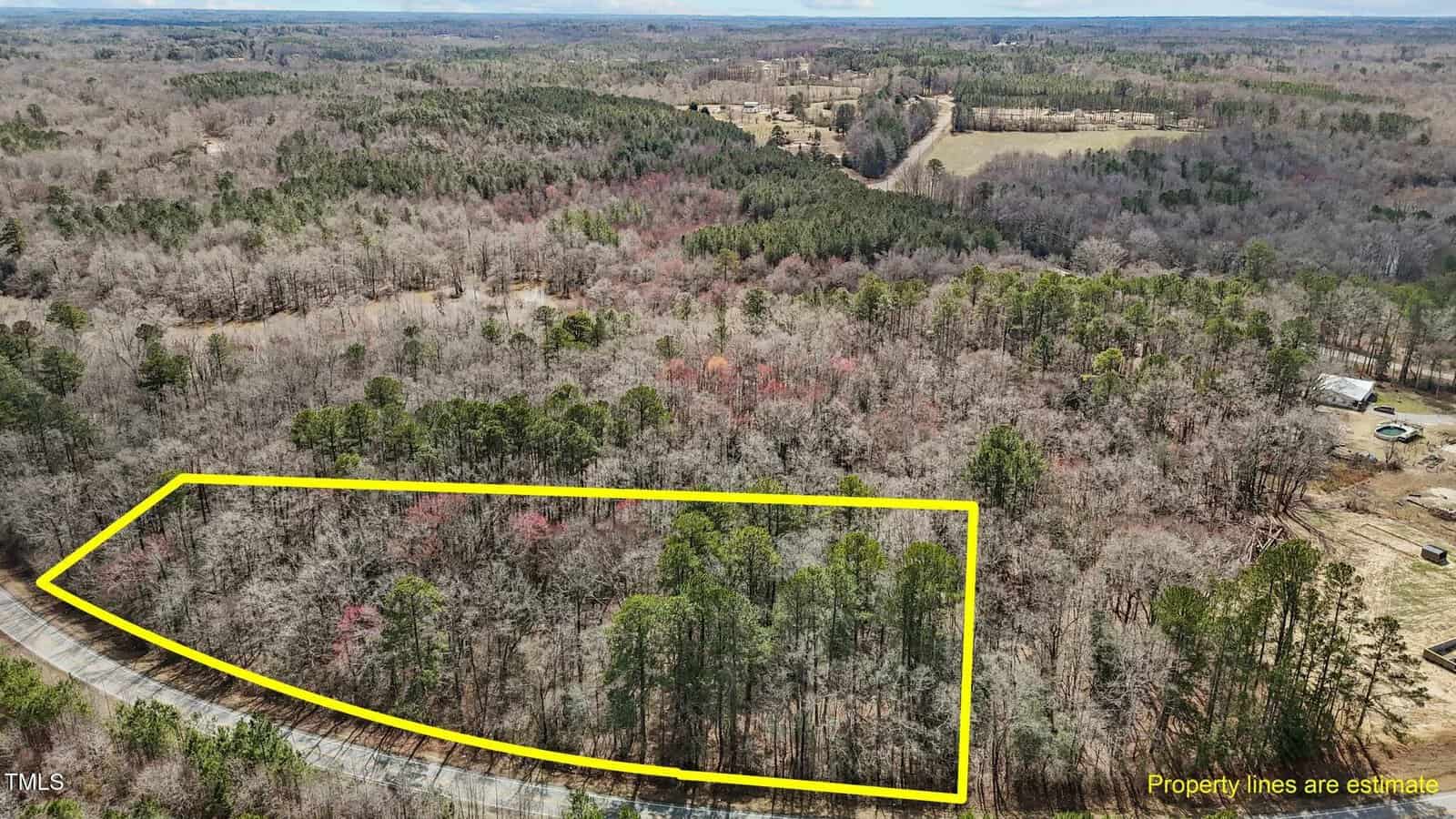 Aerial view of a wooded area in a rural landscape, with the property boundary outlined in yellow. Roads and open fields are visible in the background. Text reads, "Property lines are estimate.